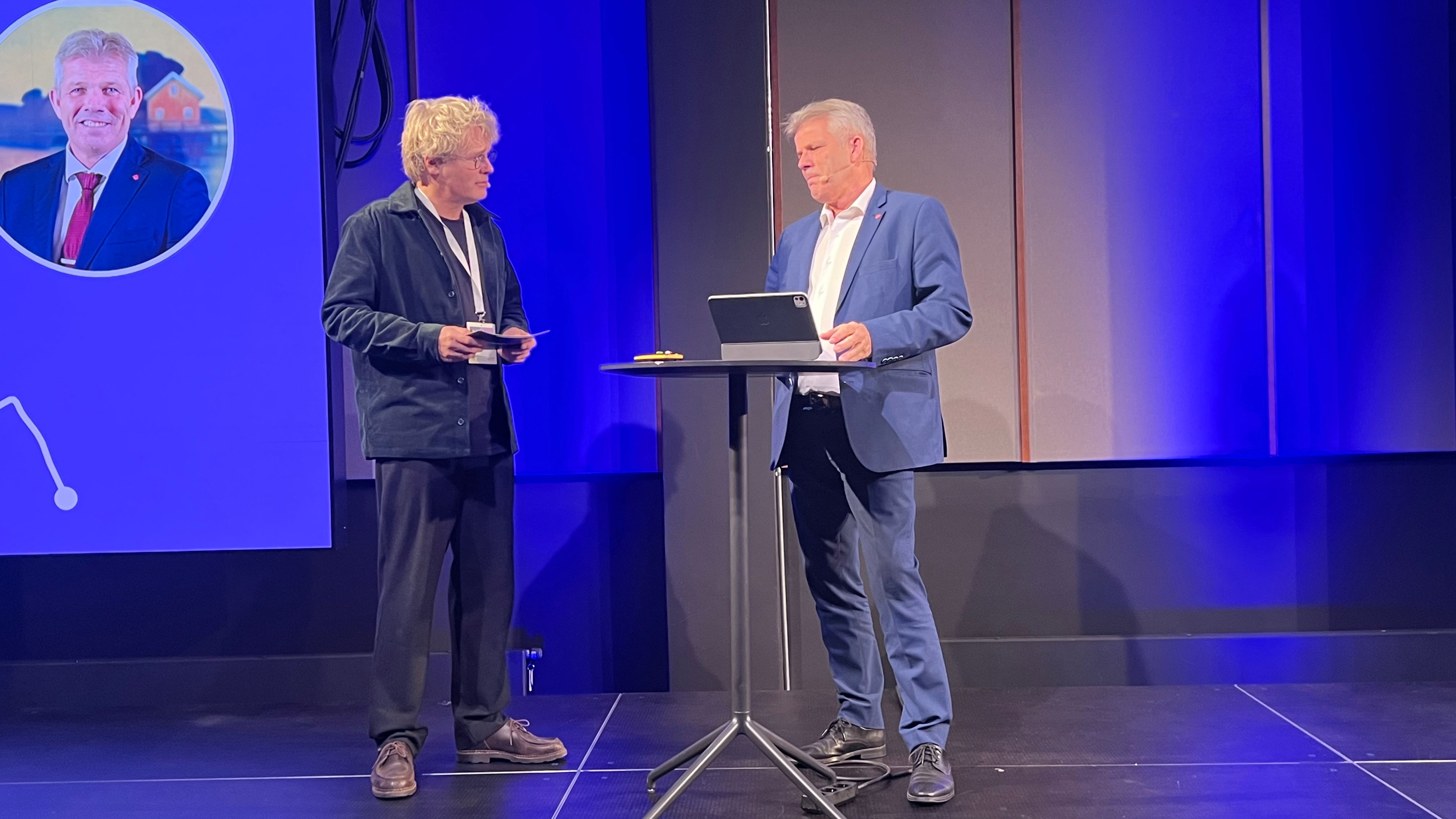 Administrerende direktør, Steinar Skjerdingstad, i Arkitektbedriftene og statsråd Bjørnar Skjæran i samtale på scenen under "By og land" i 2025. 28. april redegjør Skjæran for regjeringens videre arbeid for å nå målet i Plan for Norge om igangsetting av 130.000 nye boliger innen 2030. 