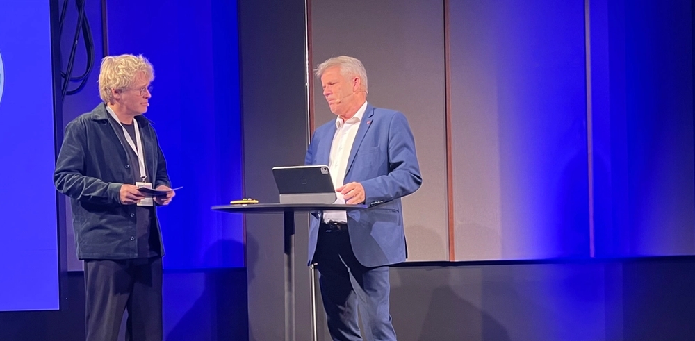 Administrerende direktør, Steinar Skjerdingstad, i Arkitektbedriftene og statsråd Bjørnar Skjæran i samtale på scenen under "By og land" i 2025. 28. april redegjør Skjæran for regjeringens videre arbeid for å nå målet i Plan for Norge om igangsetting av 130.000 nye boliger innen 2030.