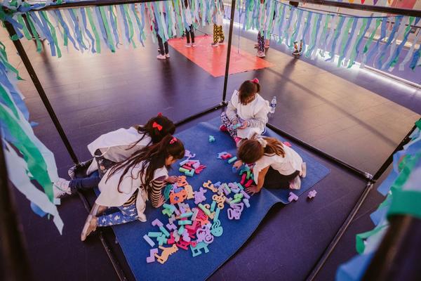 Un grupo de niñas jugando sobre una algombra con bloques dentro de una estructura.