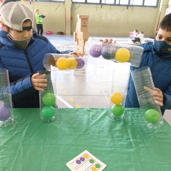 Dos niños jugando con pelotas de colores en recipientes de plástico.
