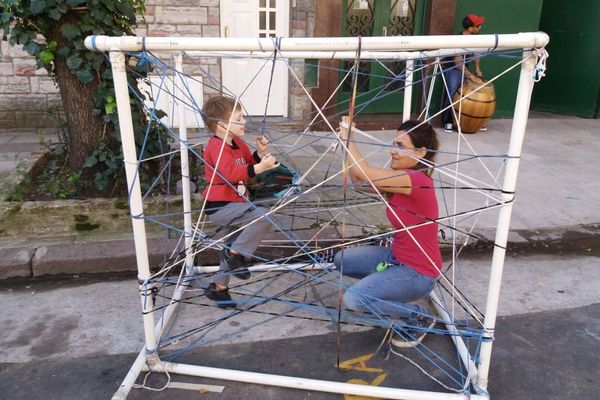 Una mujer y un niño jugando en una estructura hecha de caños y cuerdas en la calle.