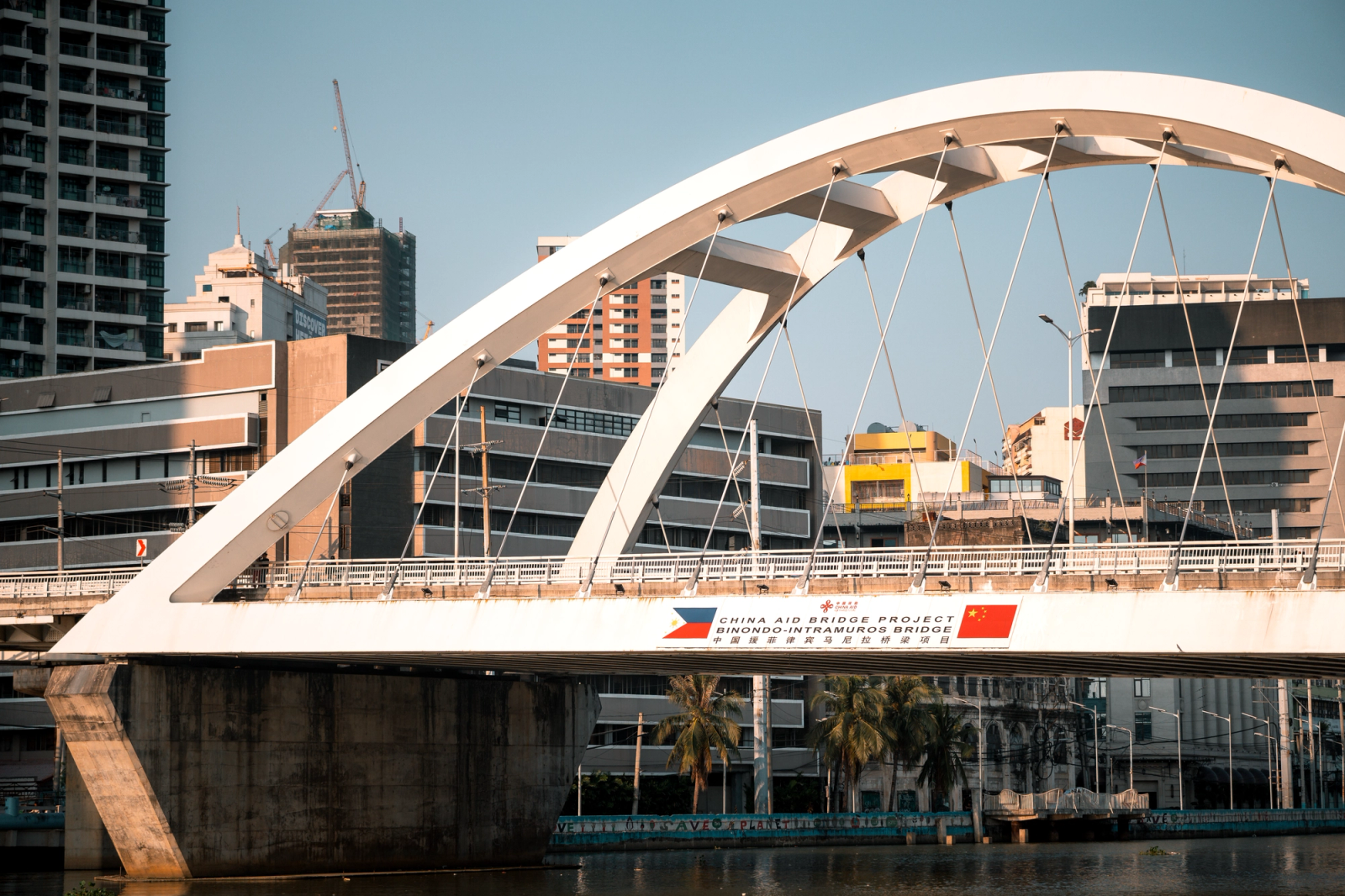 A white arched bridge crossing a river through a modern skyline