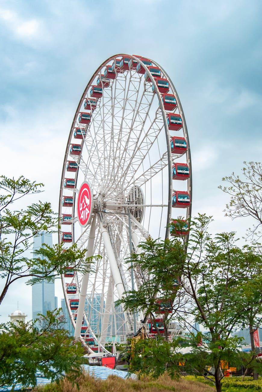 Large ferris wheel rising above trees with a city skyline behind