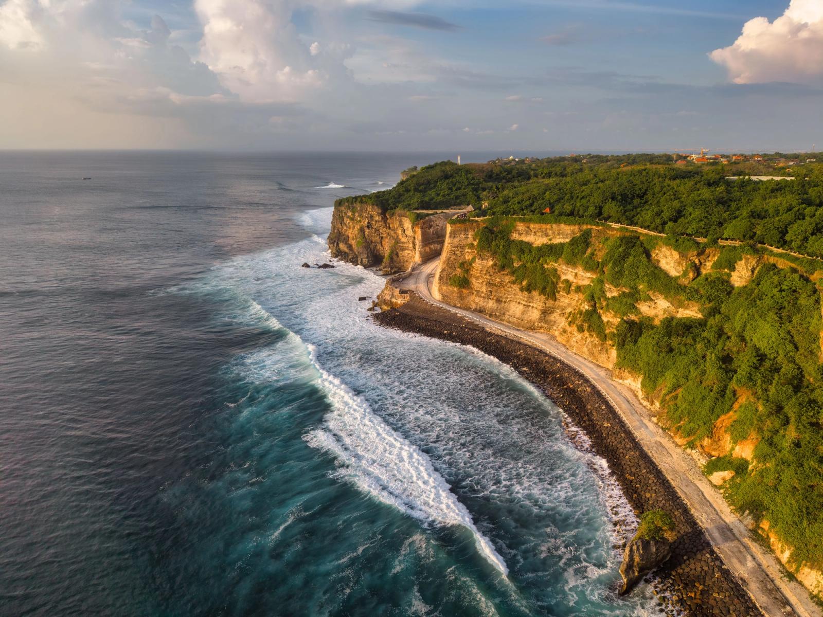 Breathtaking aerial view of Uluwatu cliffs and ocean waves in Bali, Indonesia during a sunny day