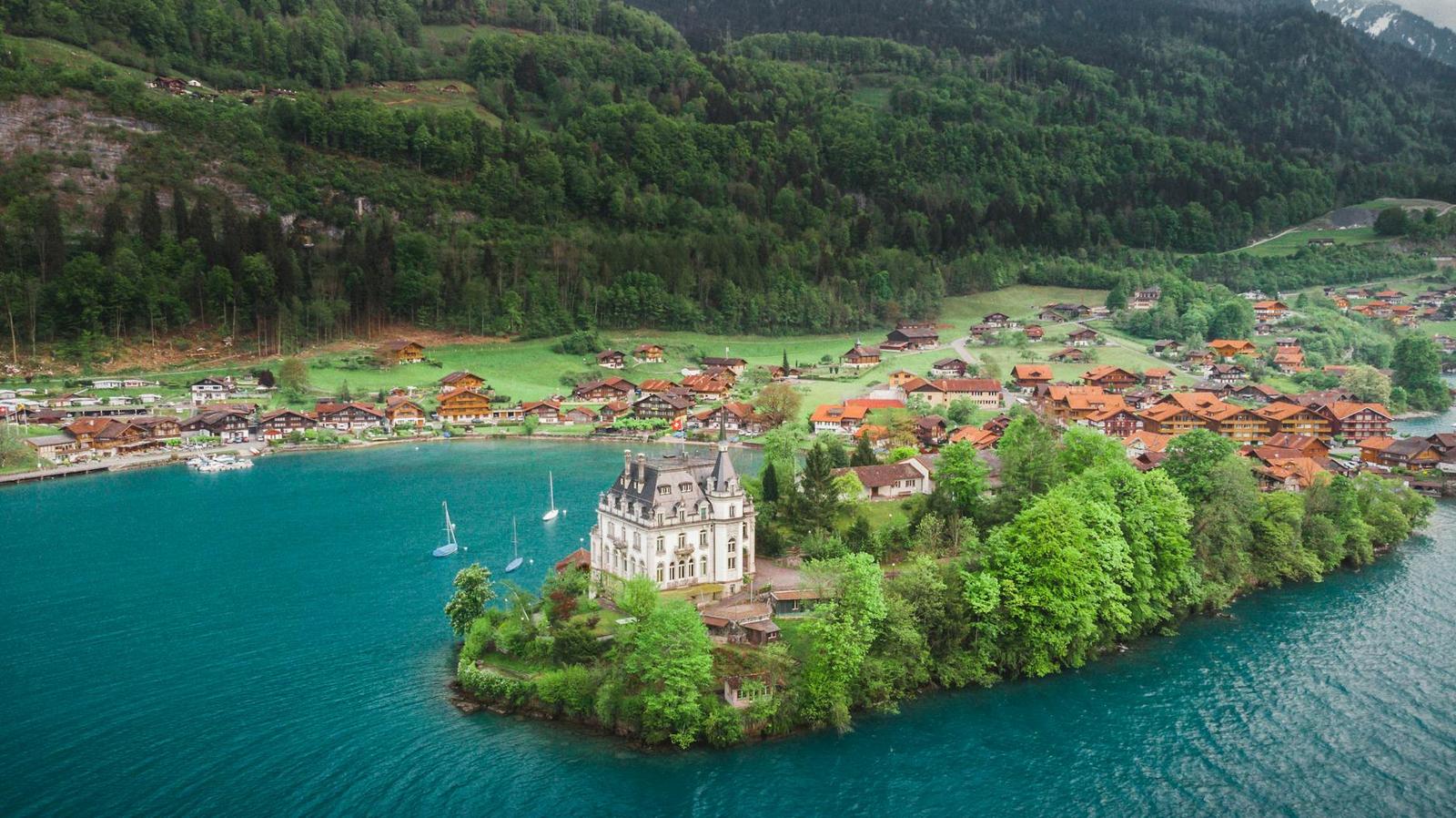 Turreted lakeside mansion on a small peninsula beside a green-hilled village