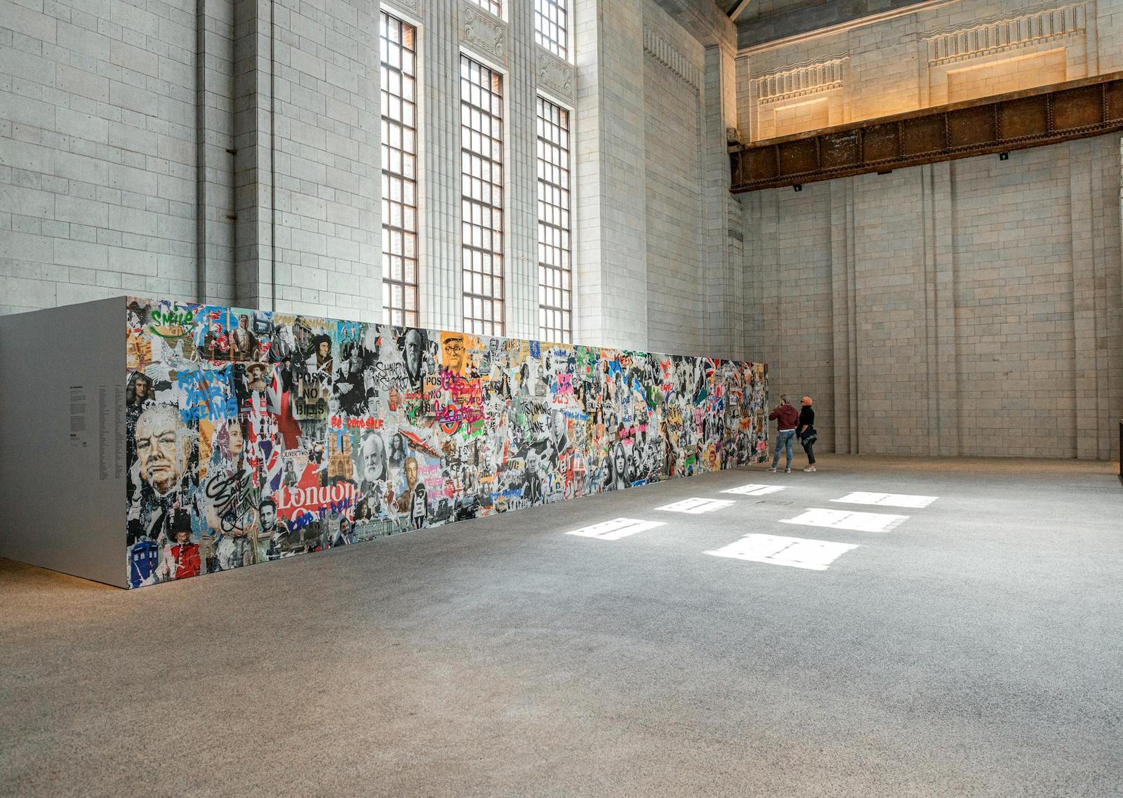 Visitors viewing a long mural collage inside a converted industrial hall