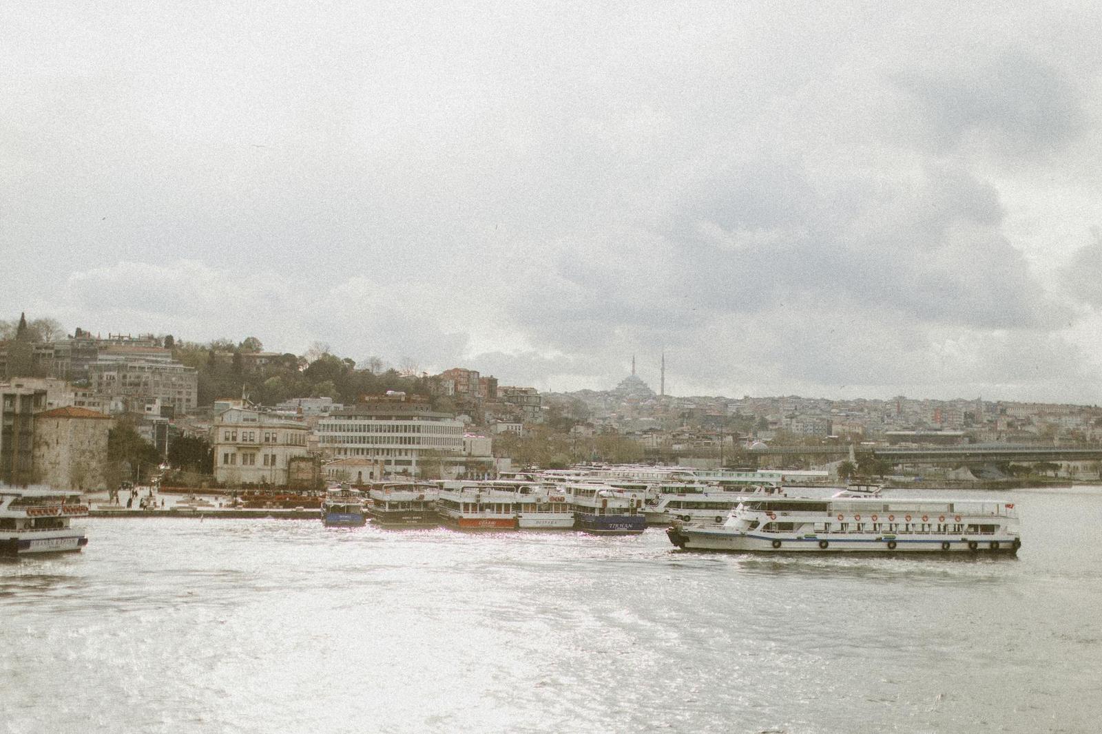 Ferries moored along a waterfront beneath a hazy hillside skyline