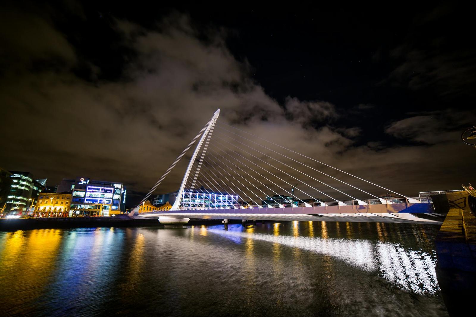 A harp-shaped suspension bridge lit up at night over a river
