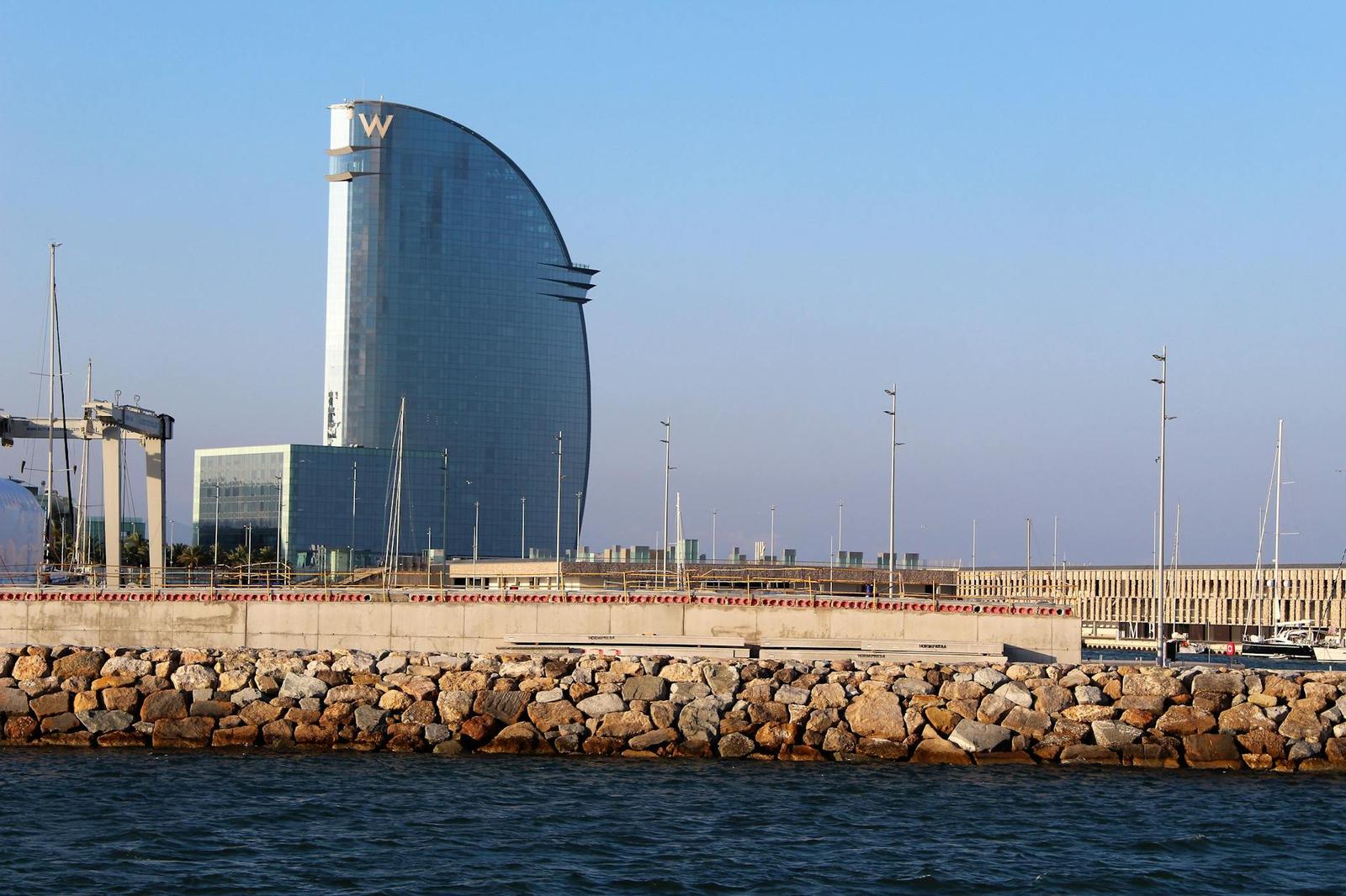 A sail-shaped waterfront hotel tower rises beyond a rocky breakwater