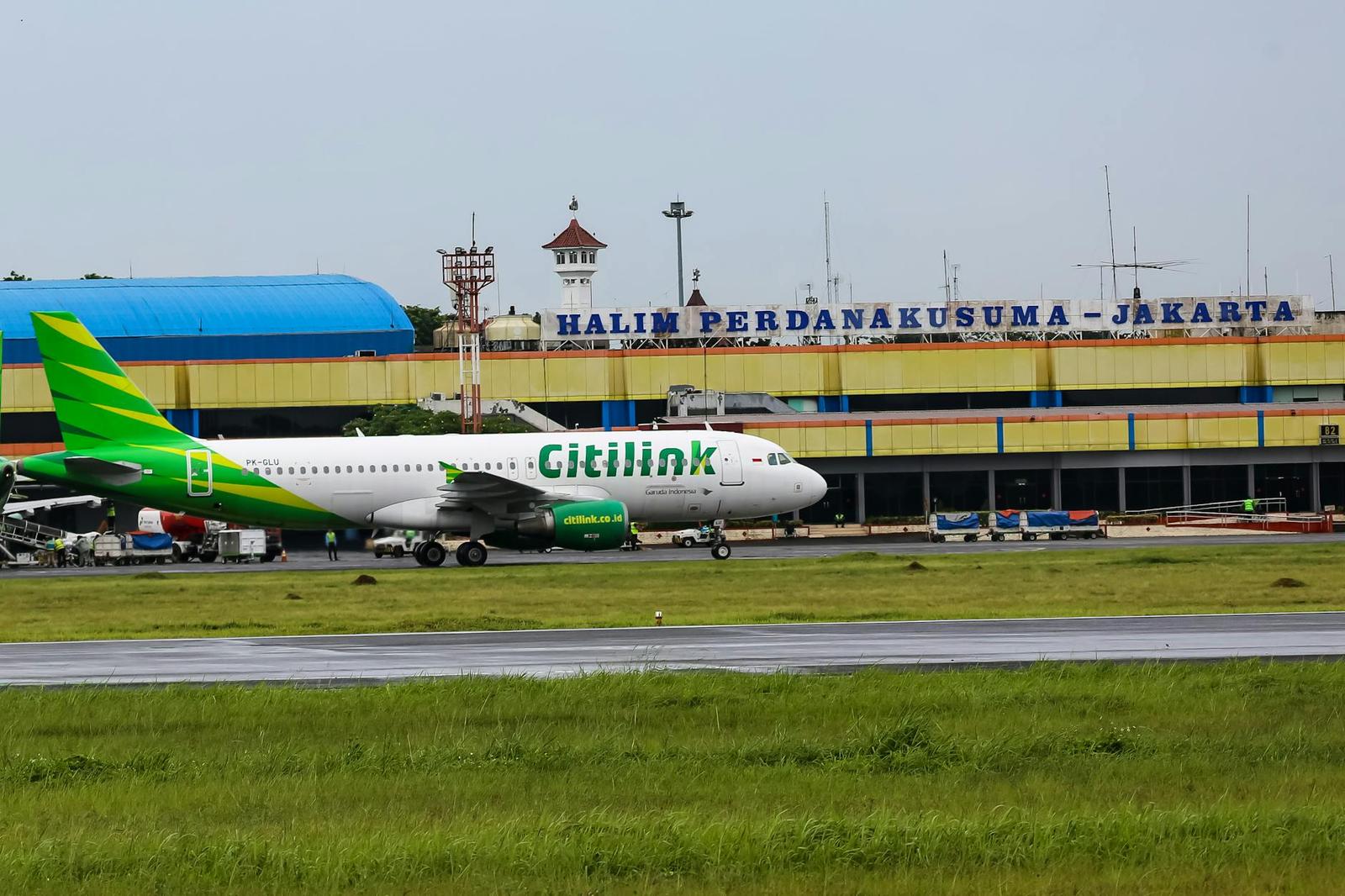 A green and white airliner taxis past a terminal building signed for Jakarta