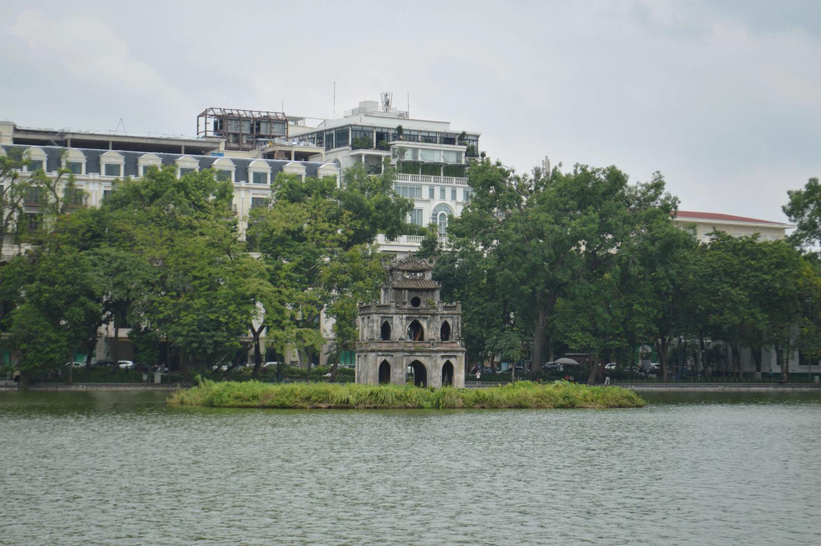 Scenic view of Turtle Tower on Hoan Kiem Lake surrounded by lush greenery and historic buildings in Hanoi, Vietnam