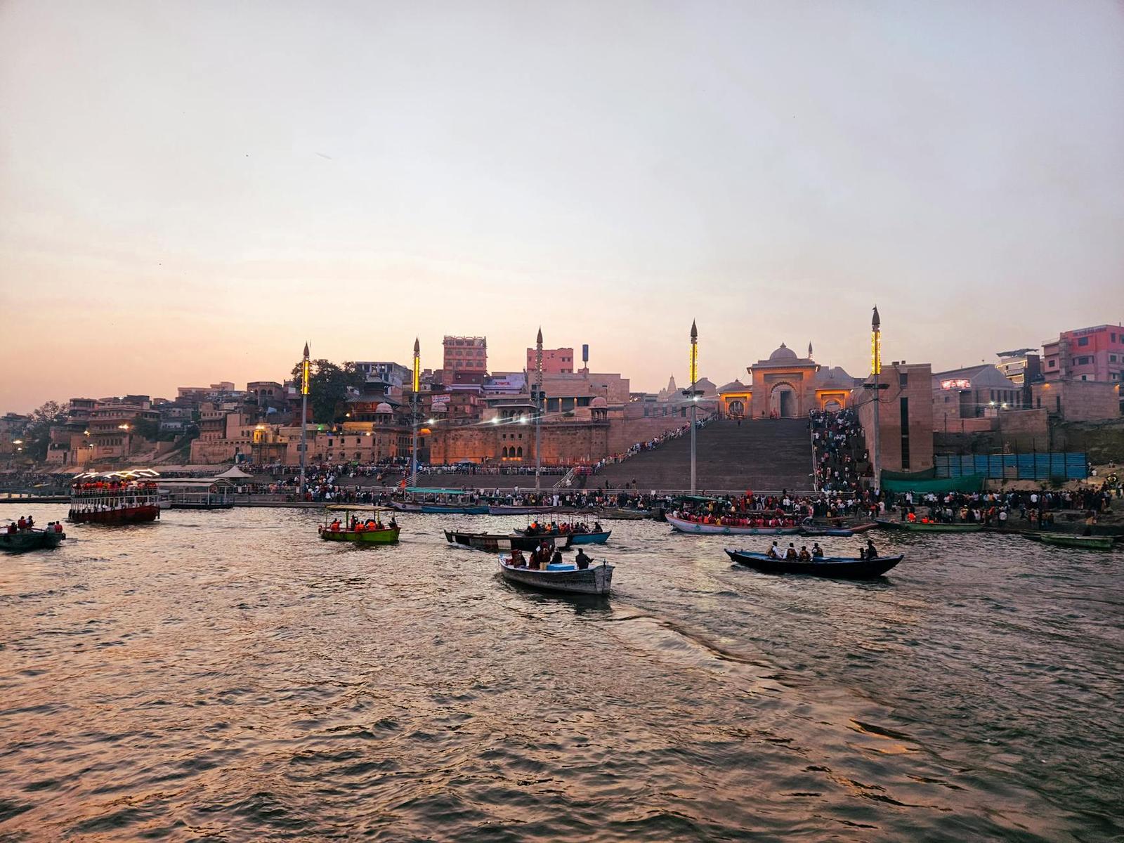 Boats crowded with passengers on a river at dusk with a temple-lined shore behind