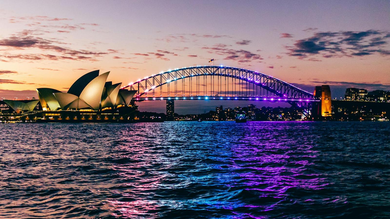 Vibrant sunset view of Sydney's iconic Opera House and illuminated Harbor Bridge reflecting on water