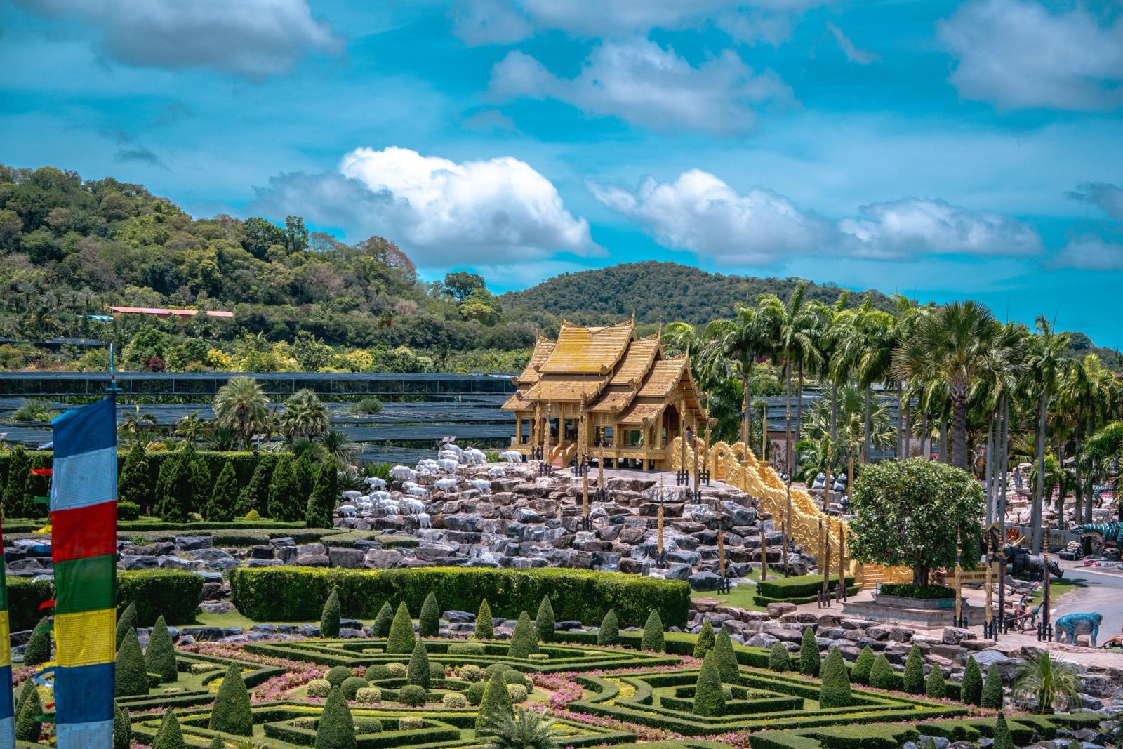 A golden temple pavilion set among manicured topiary gardens with prayer flags