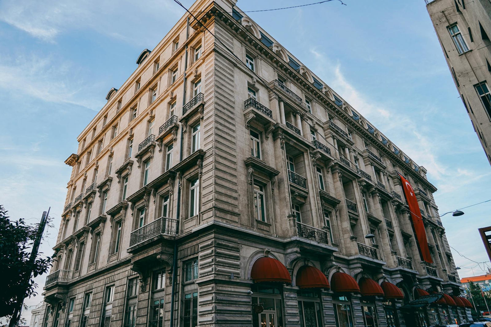 Grand stone corner hotel with balconies and red awnings over the entrance