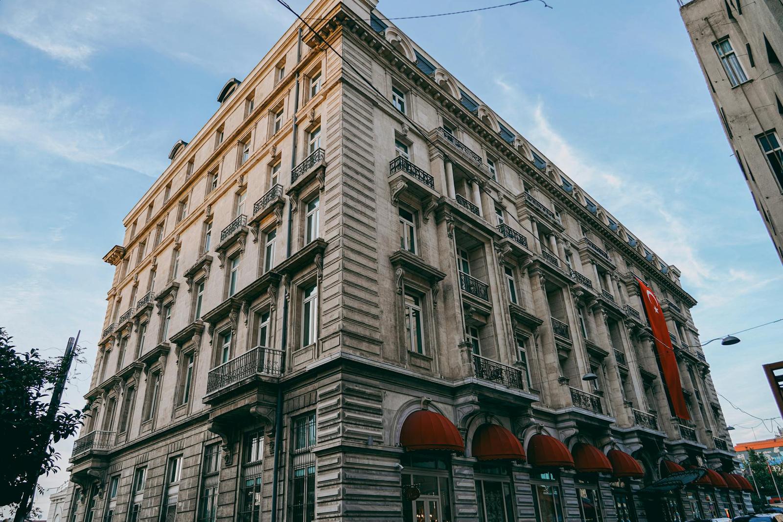 Grand stone corner hotel with balconies and red awnings over the entrance