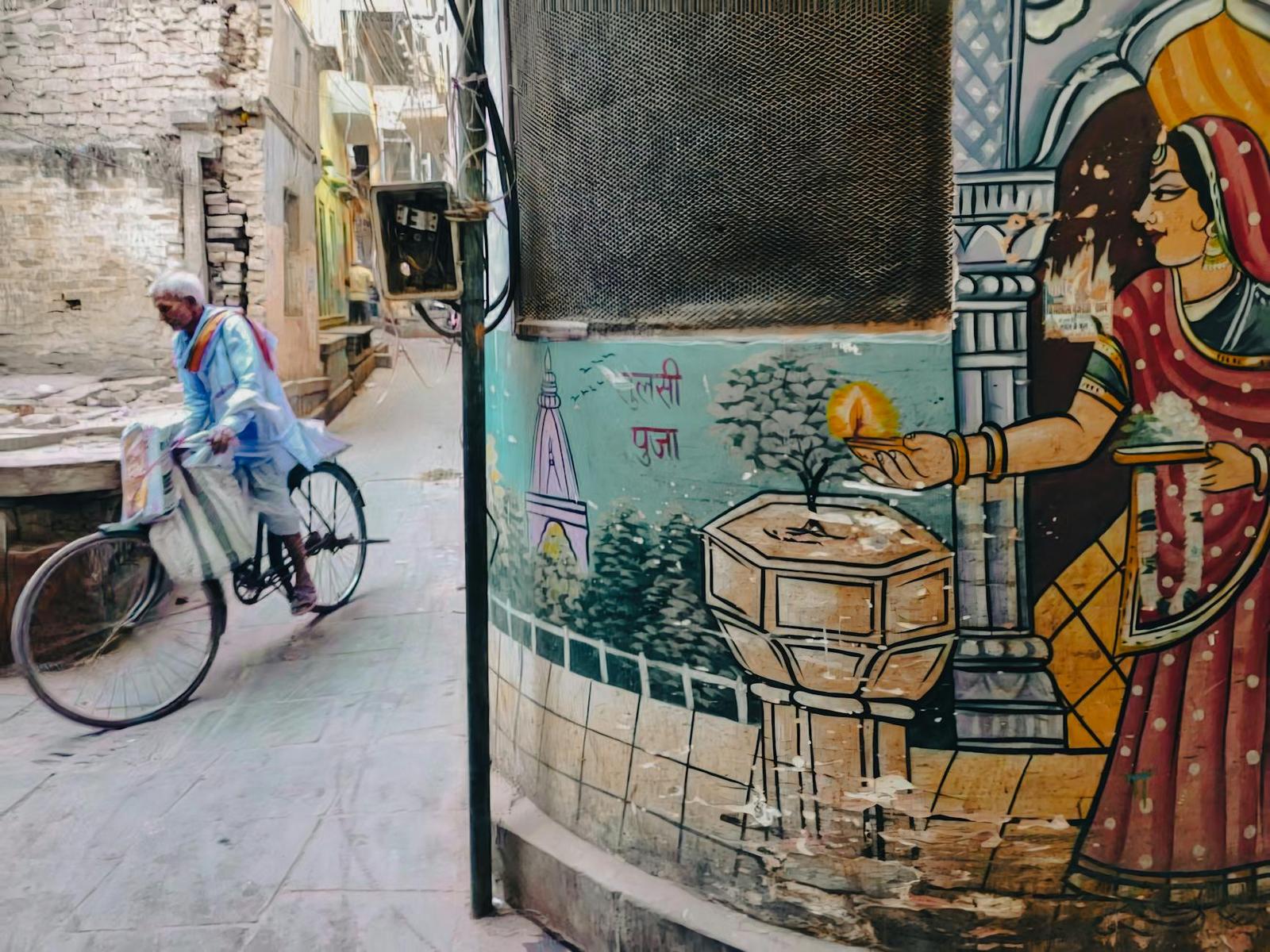 A man cycling past a painted mural in a narrow alley
