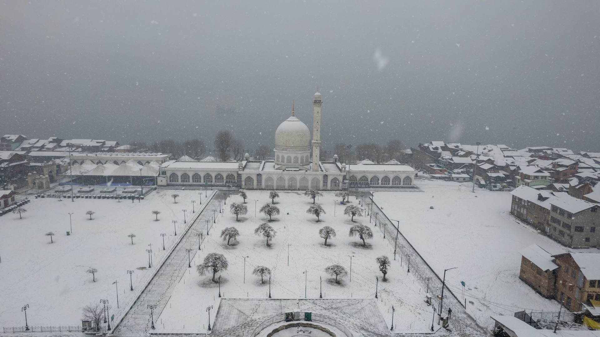 A snow-covered mosque courtyard with bare trees during a snowfall