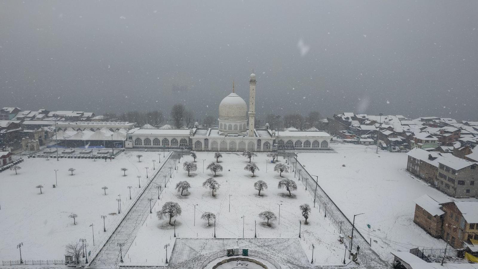 A snow-covered mosque courtyard with bare trees during a snowfall