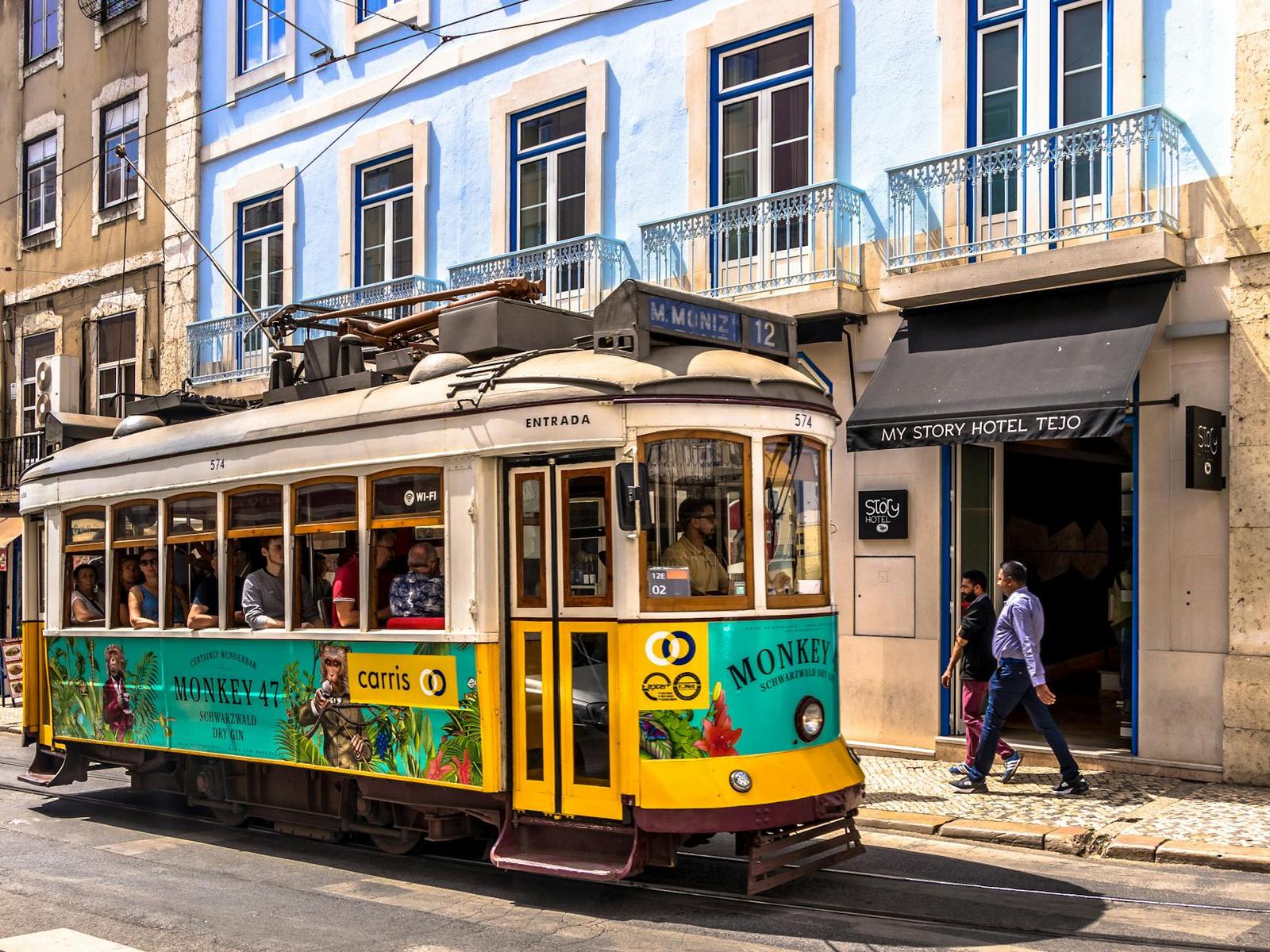 Vintage yellow tram on a narrow cobbled street with pedestrians beside a hotel entrance