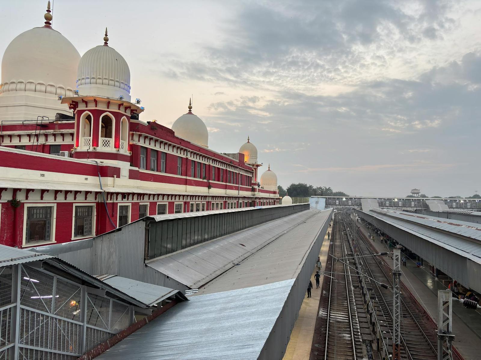 A domed red-and-white railway station building beside empty tracks under a cloudy sky