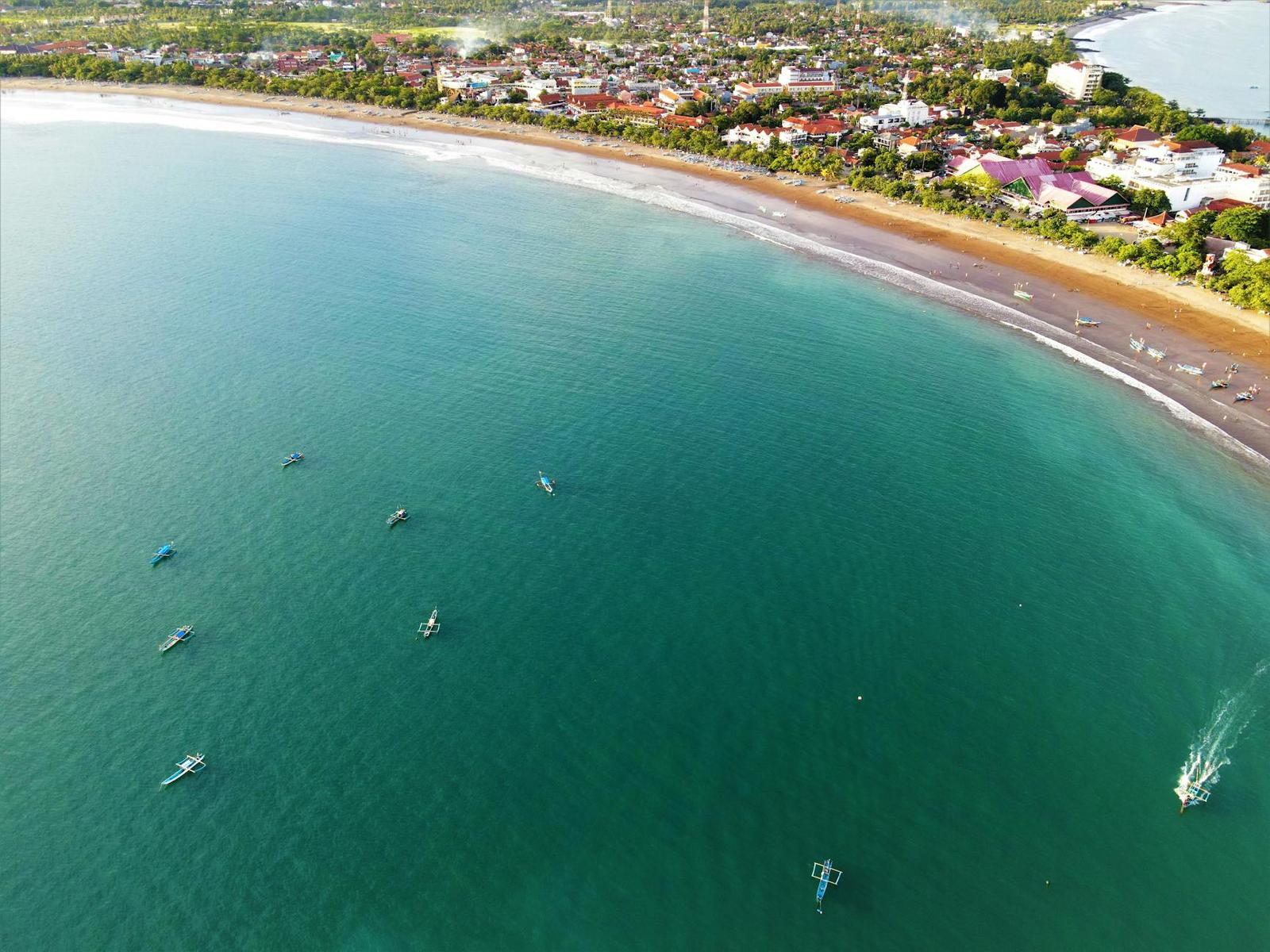 Aerial view of small fishing boats scattered across a curved turquoise bay