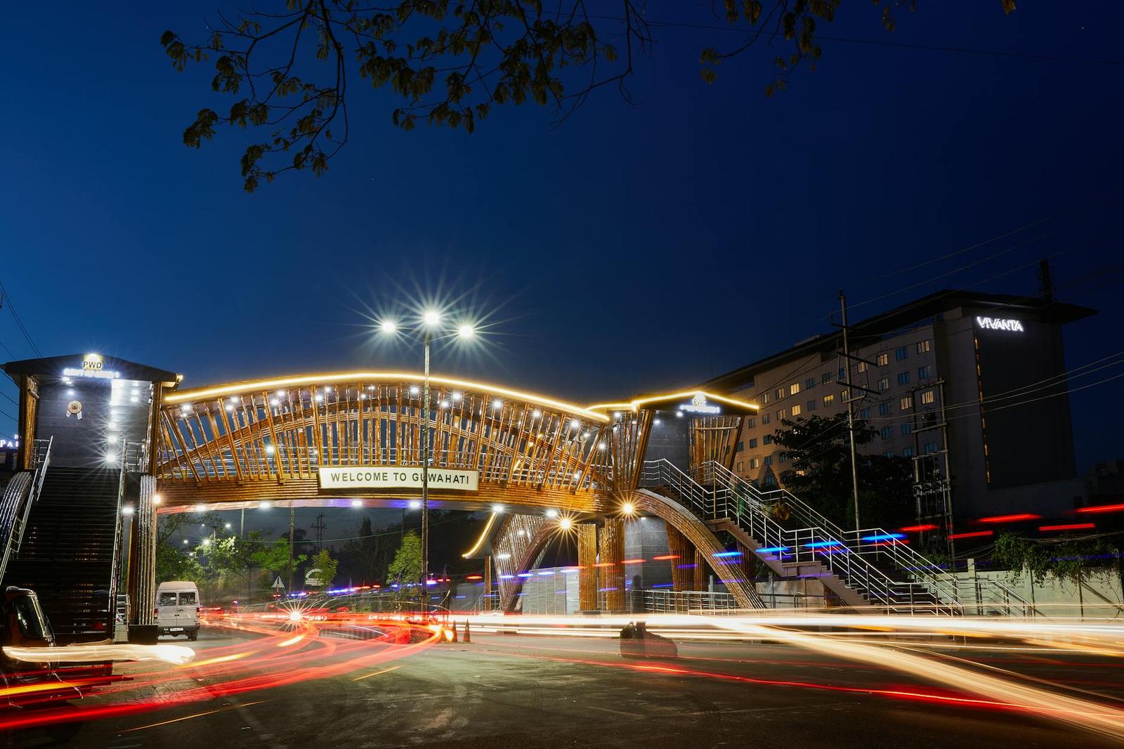 An illuminated arched pedestrian bridge over a city road at night