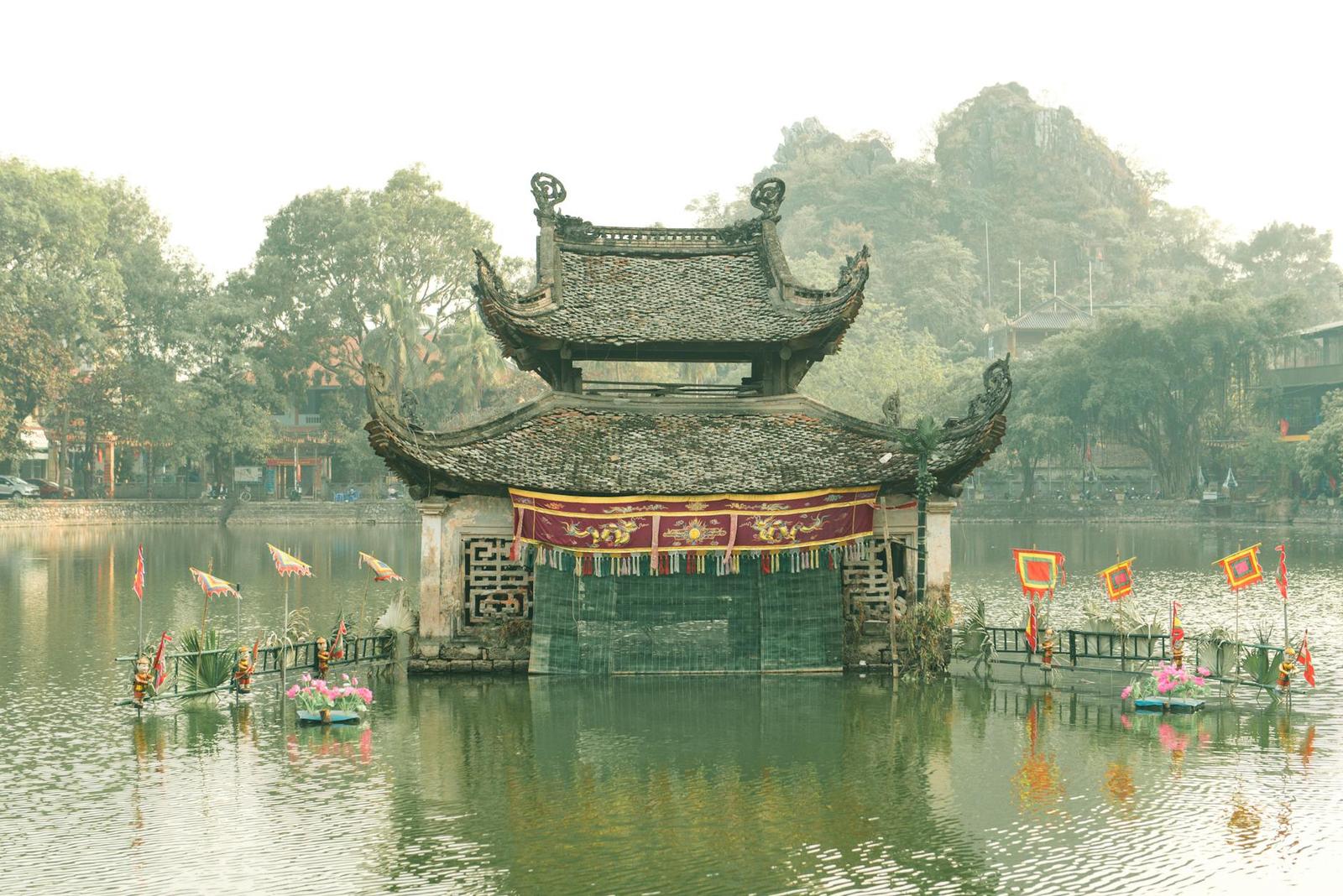 A wooden temple pavilion rising from a misty lake with small boats around it