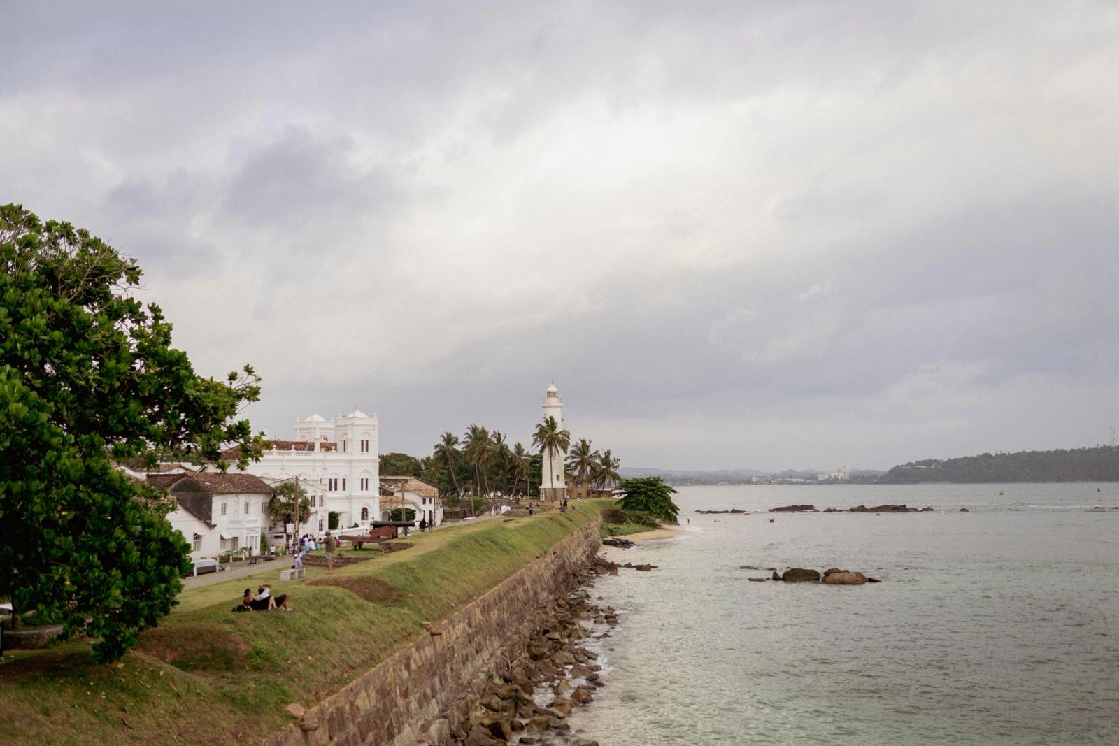 Coastal town with a white colonial building and clock tower beside a stone rampart