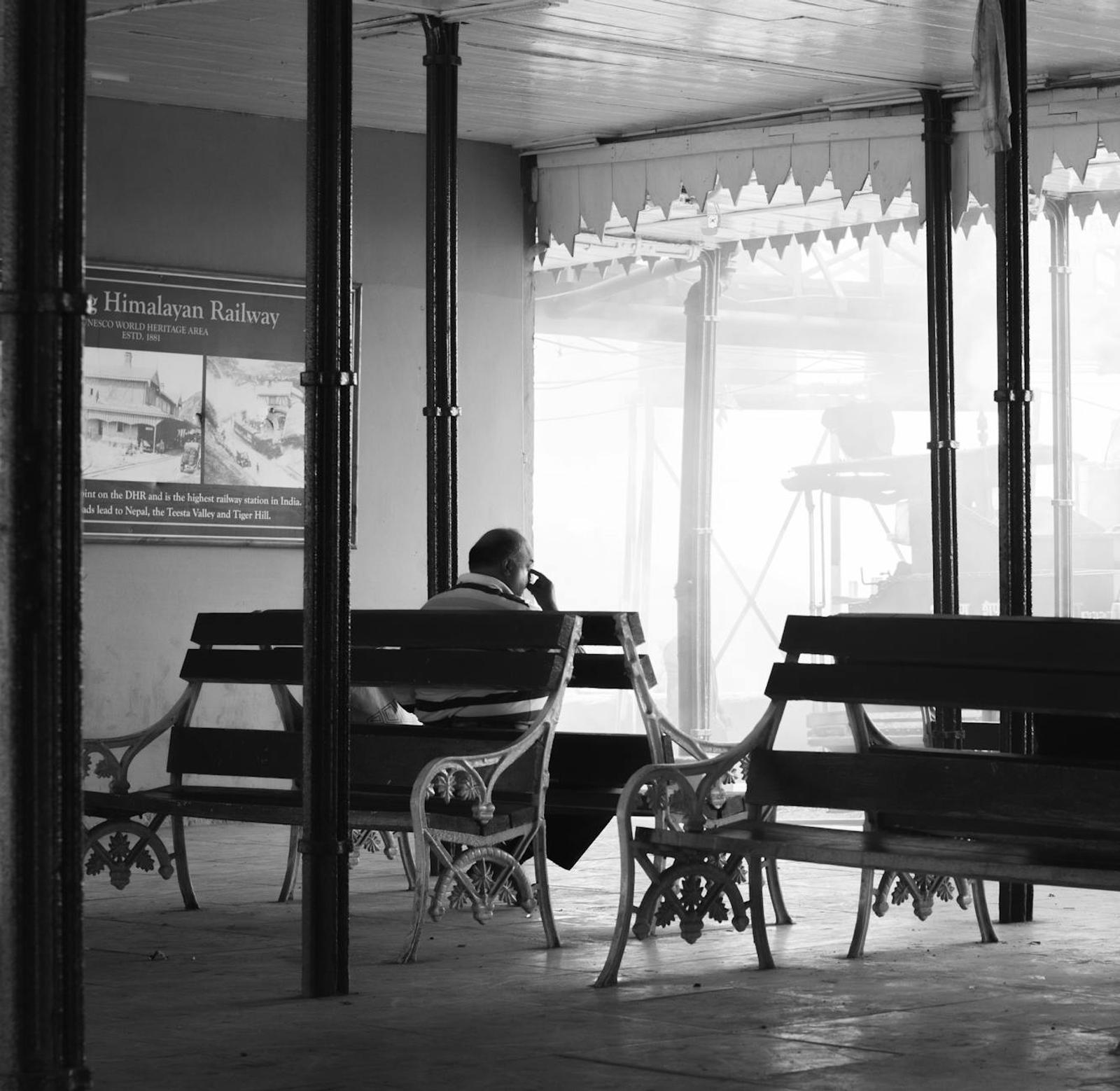 A man sits alone on a bench at the misty Darjeeling Railway Station