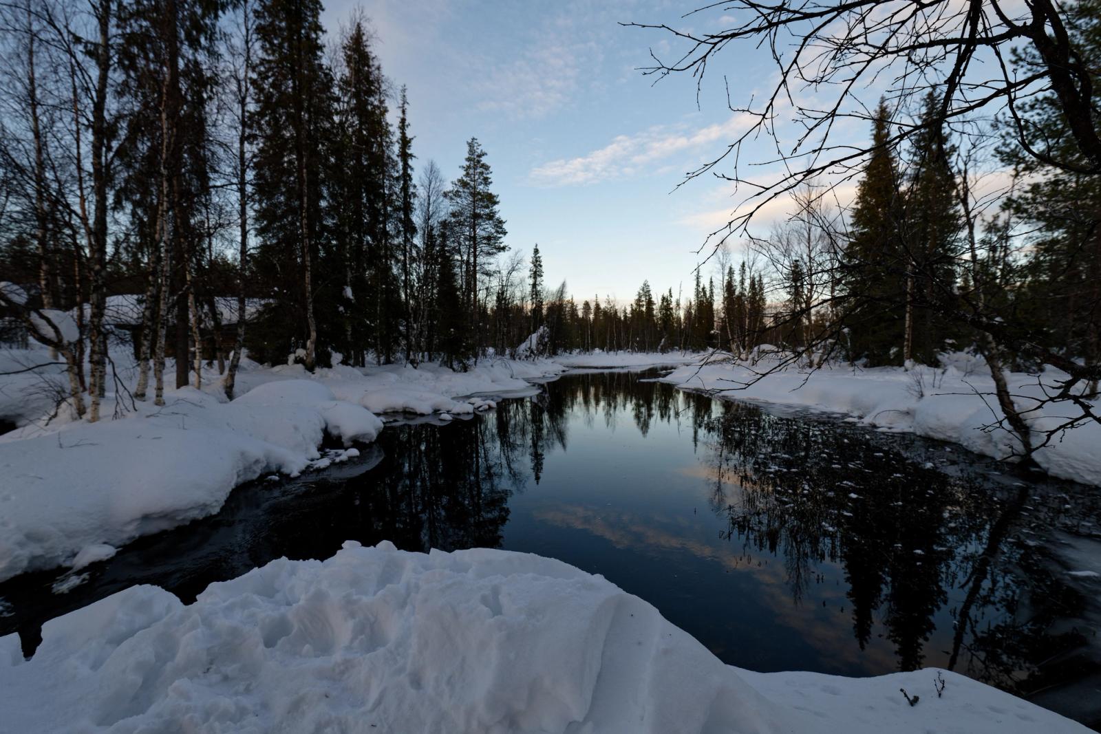 Serene winter forest river with snow and reflections in Muonio, Finland
