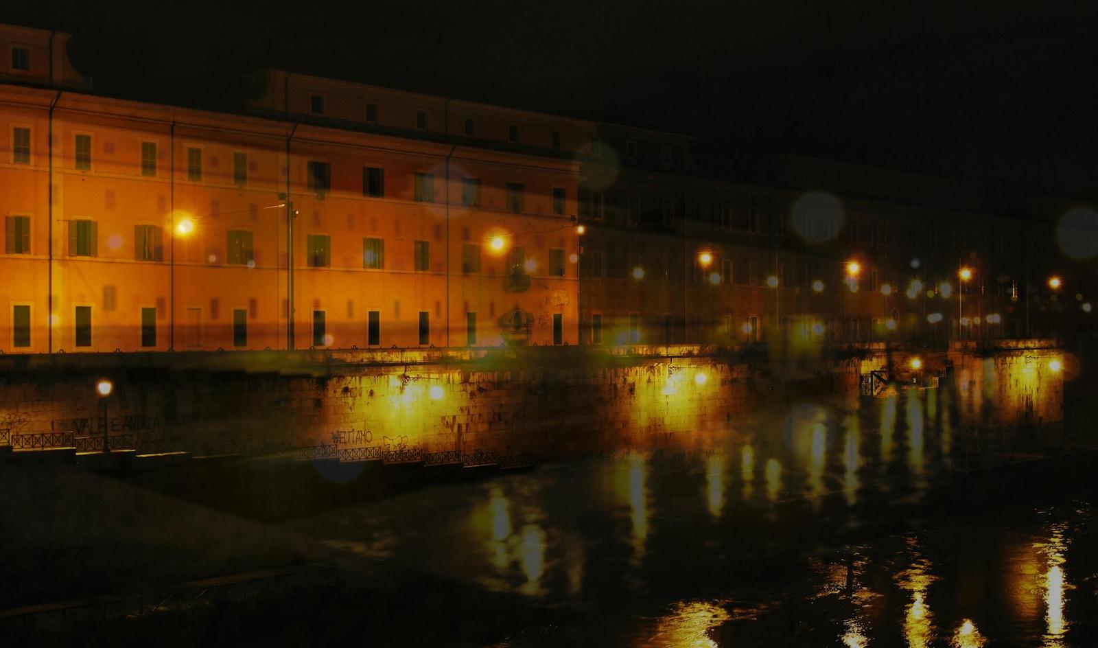 A riverside row of illuminated buildings reflected in dark water at night