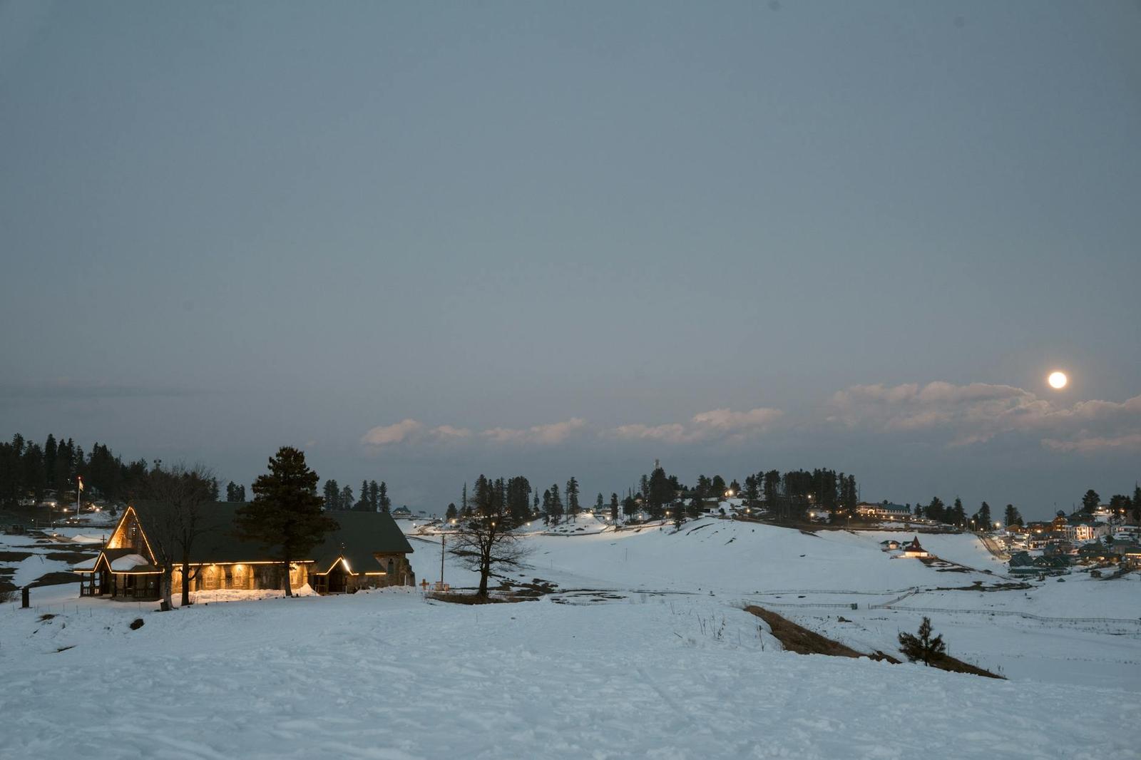 Snow-covered cabins glowing at dusk beneath a rising moon