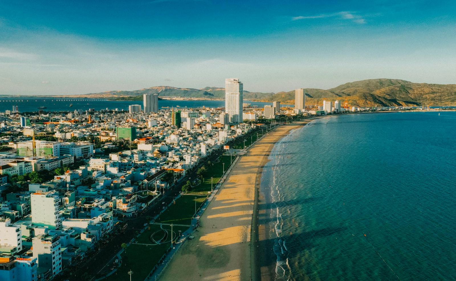 Aerial view of a curved coastal city beach with skyscrapers and hills behind