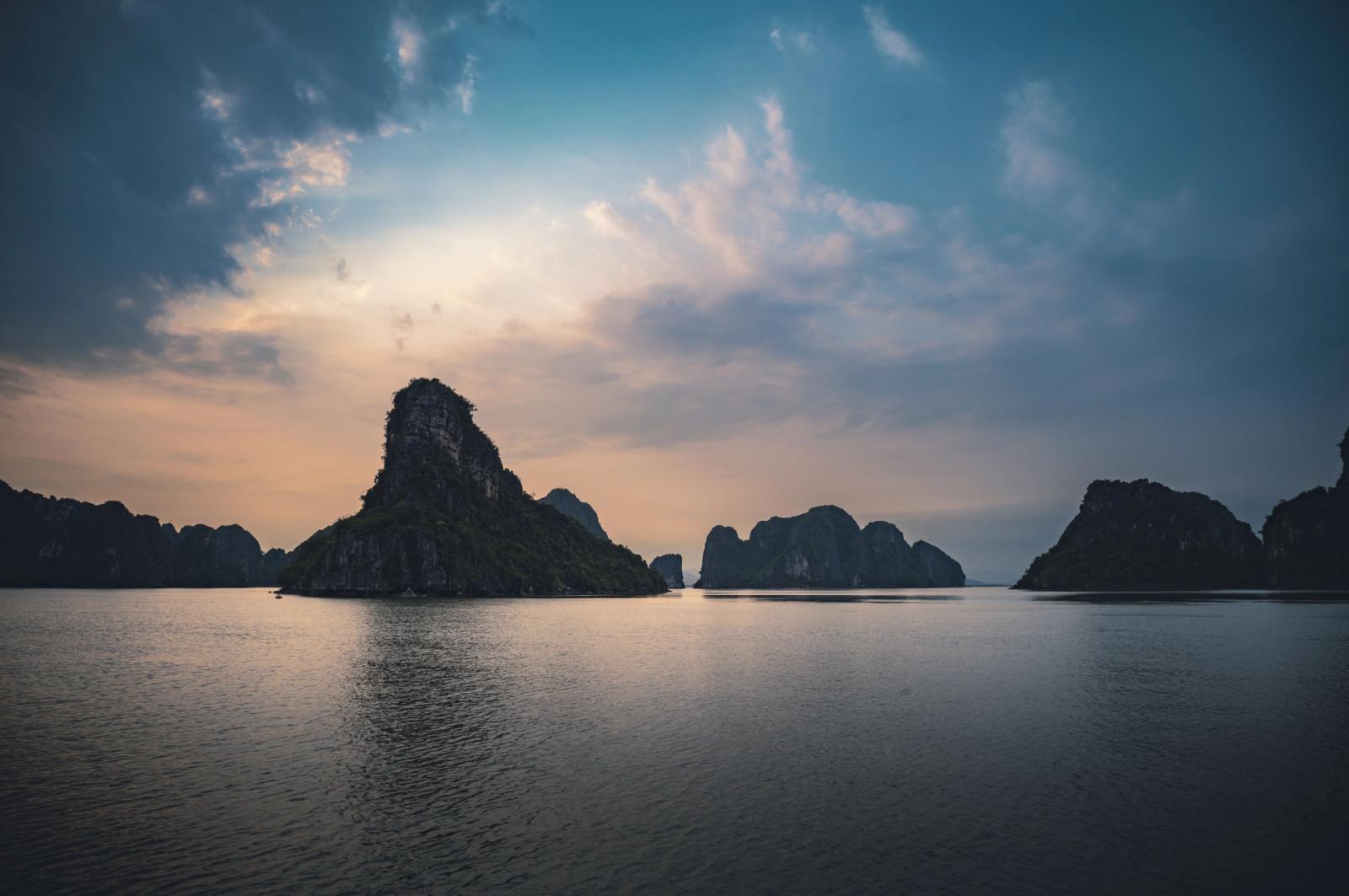 Stunning sunset over Halong Bay, Vietnam, with karst formations reflected in the tranquil waters