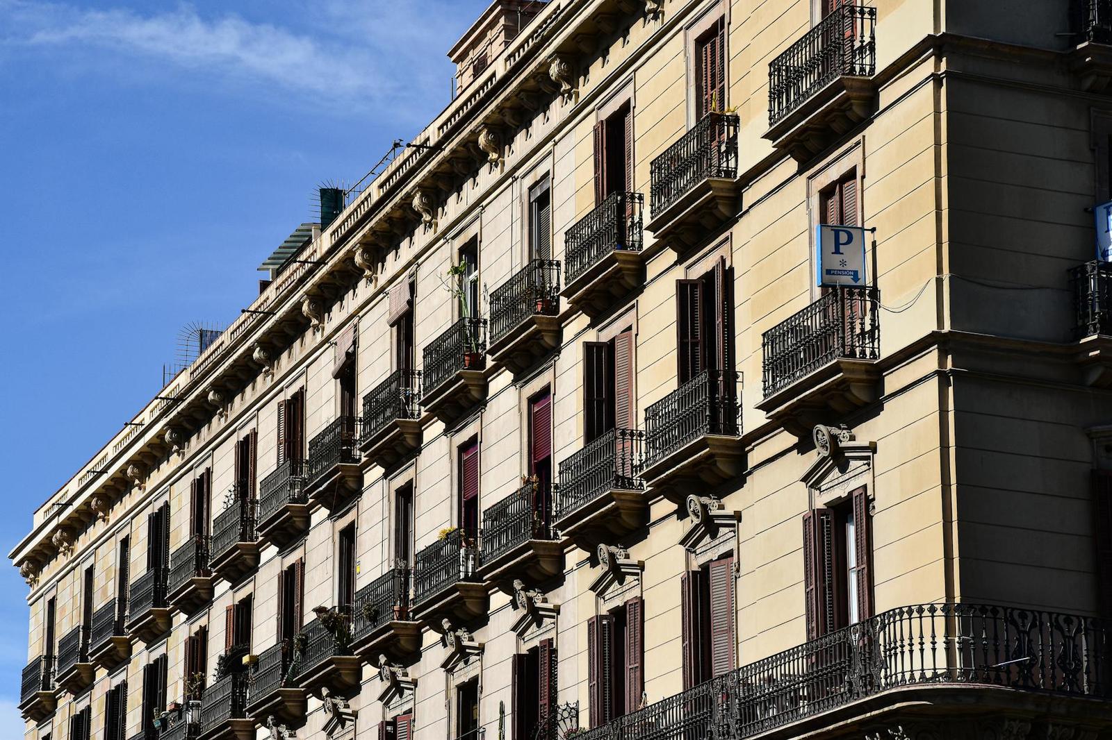 Rows of wrought-iron balconies line a classical apartment facade against blue sky