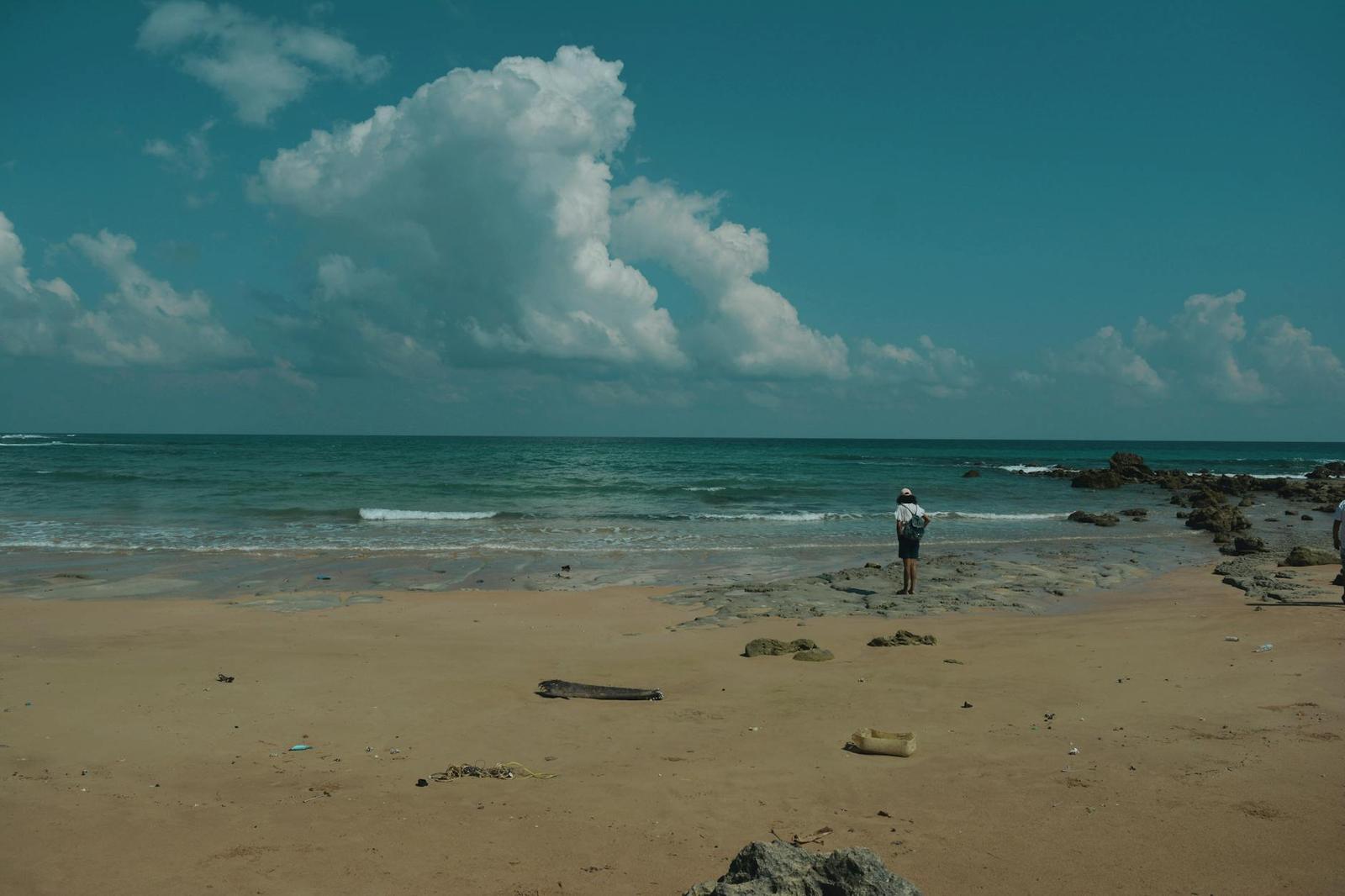 A person standing alone on a wide beach beneath a large cumulus cloud