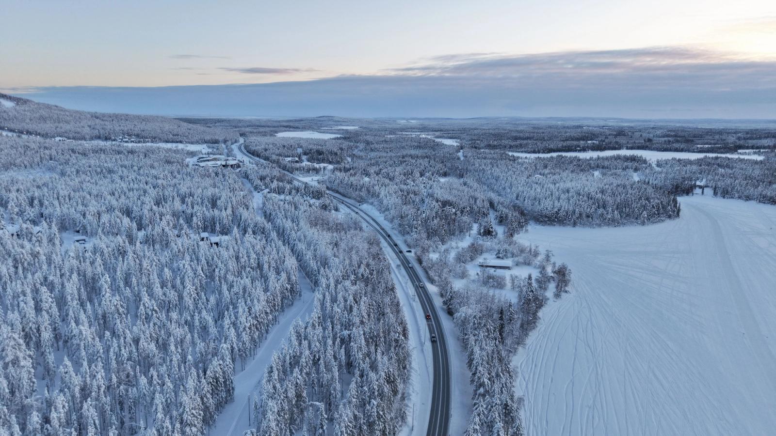 Aerial view of a snow-lined road cutting through a winter forest
