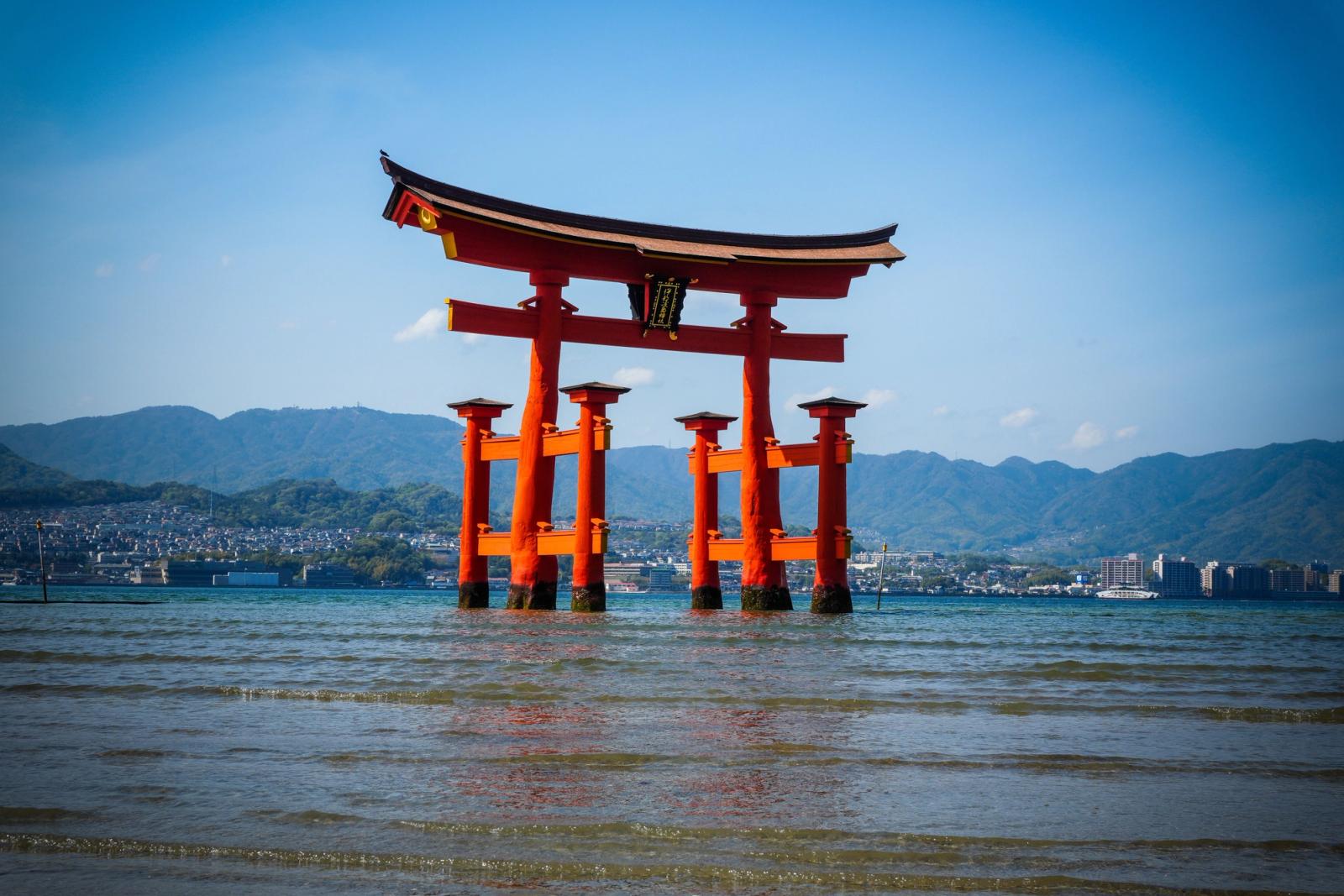 Scenic view of the iconic Itsukushima Shrine torii gate in Hiroshima, Japan, set against mountains and ocean