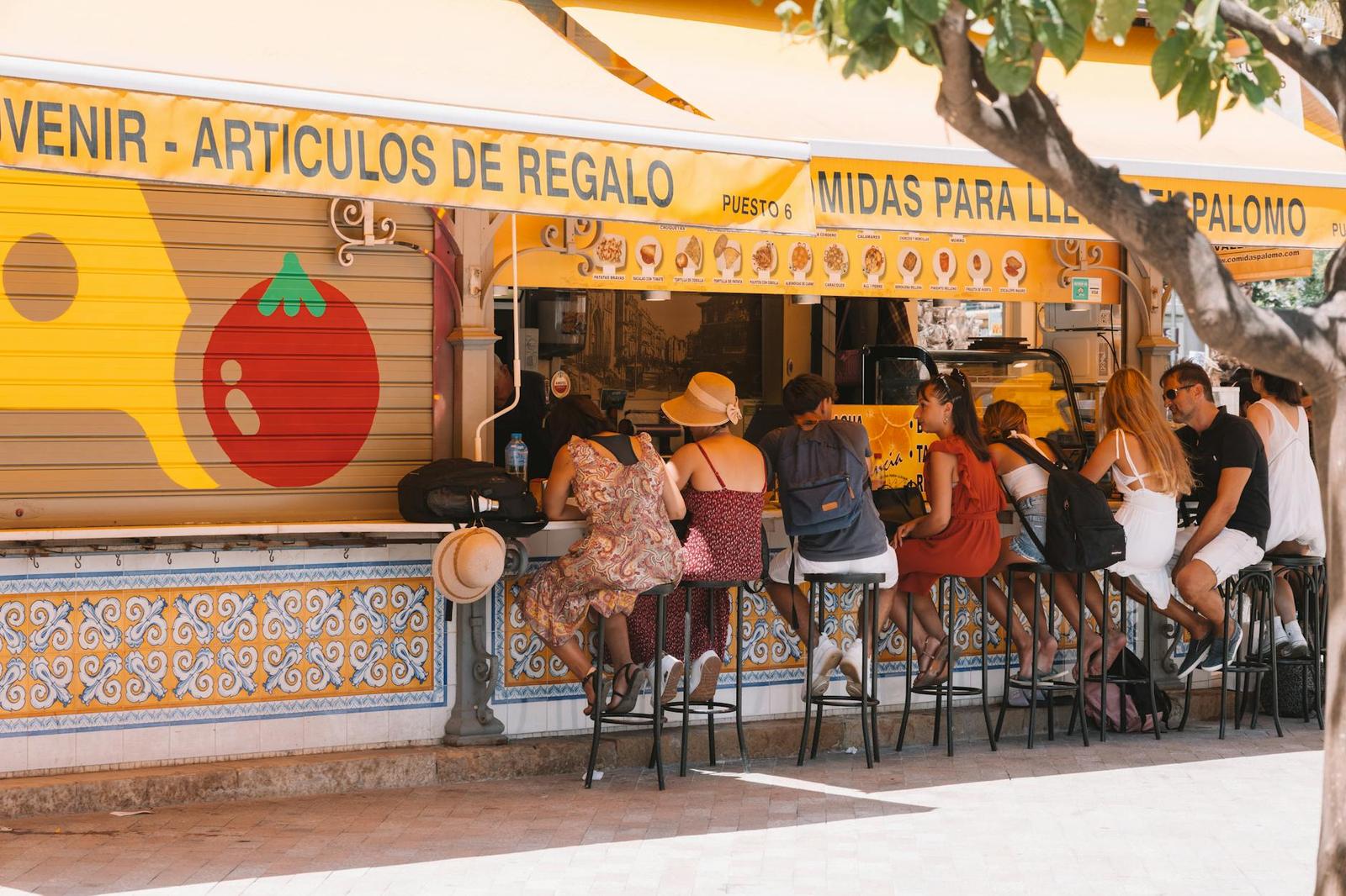 People gathered at an outdoor bar counter beneath a striped awning