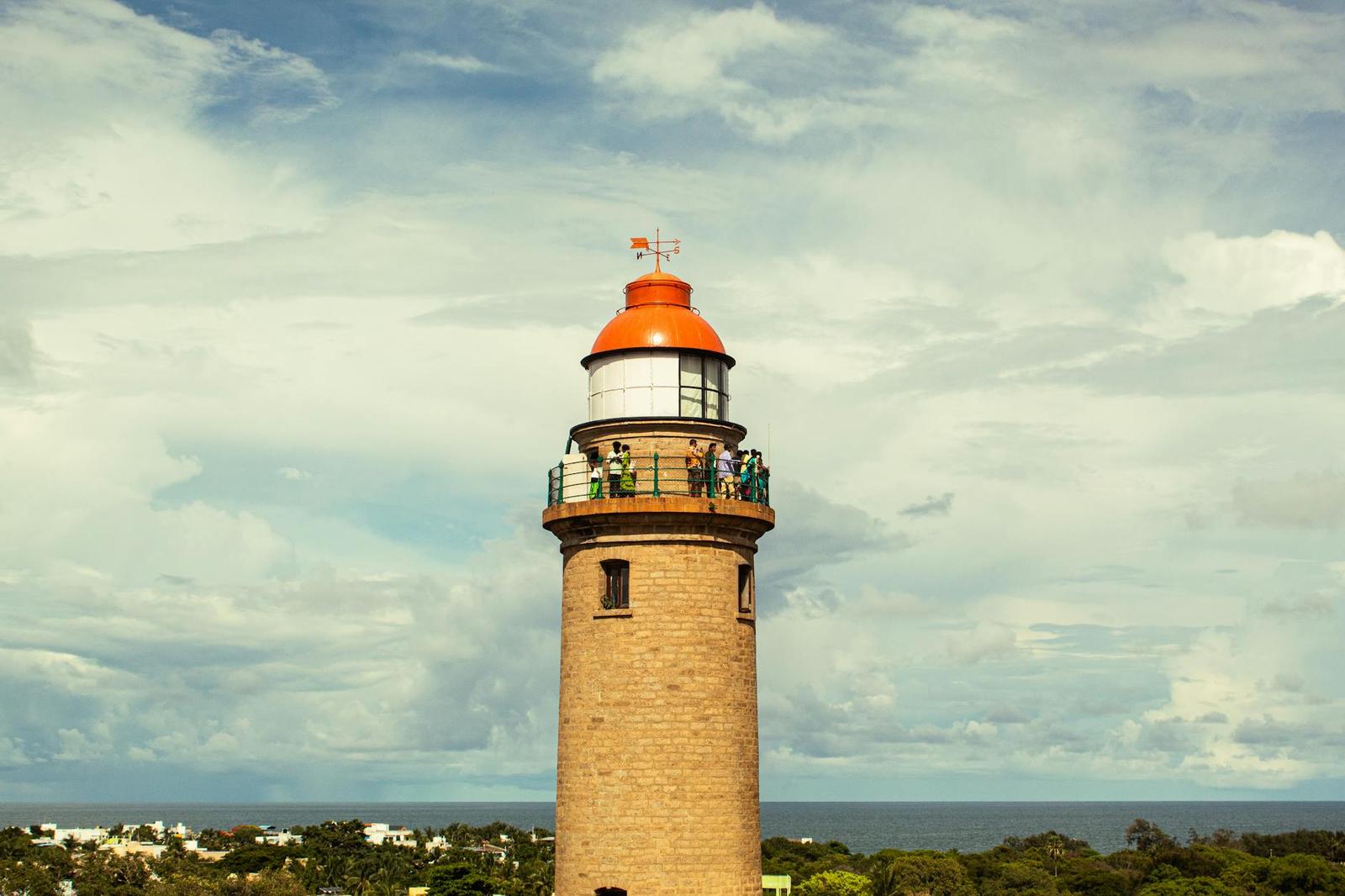 A tall stone lighthouse with an orange dome and visitors on its balcony