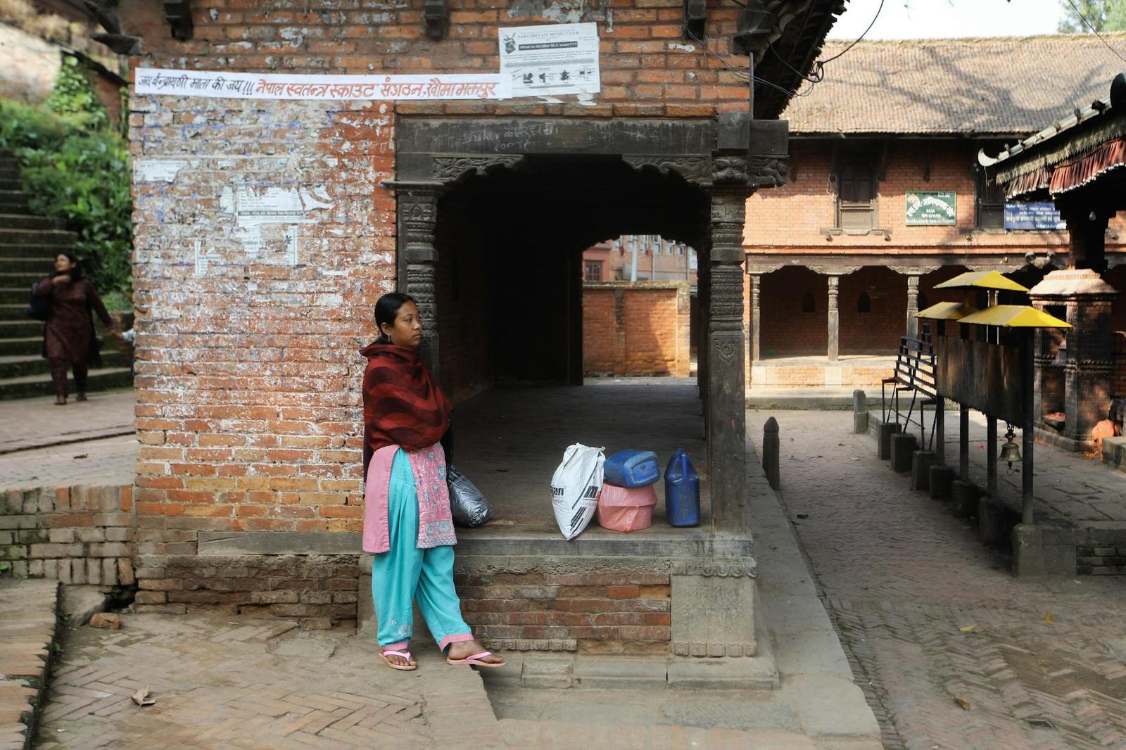 A woman sitting on the steps of a brick temple gateway with belongings beside her