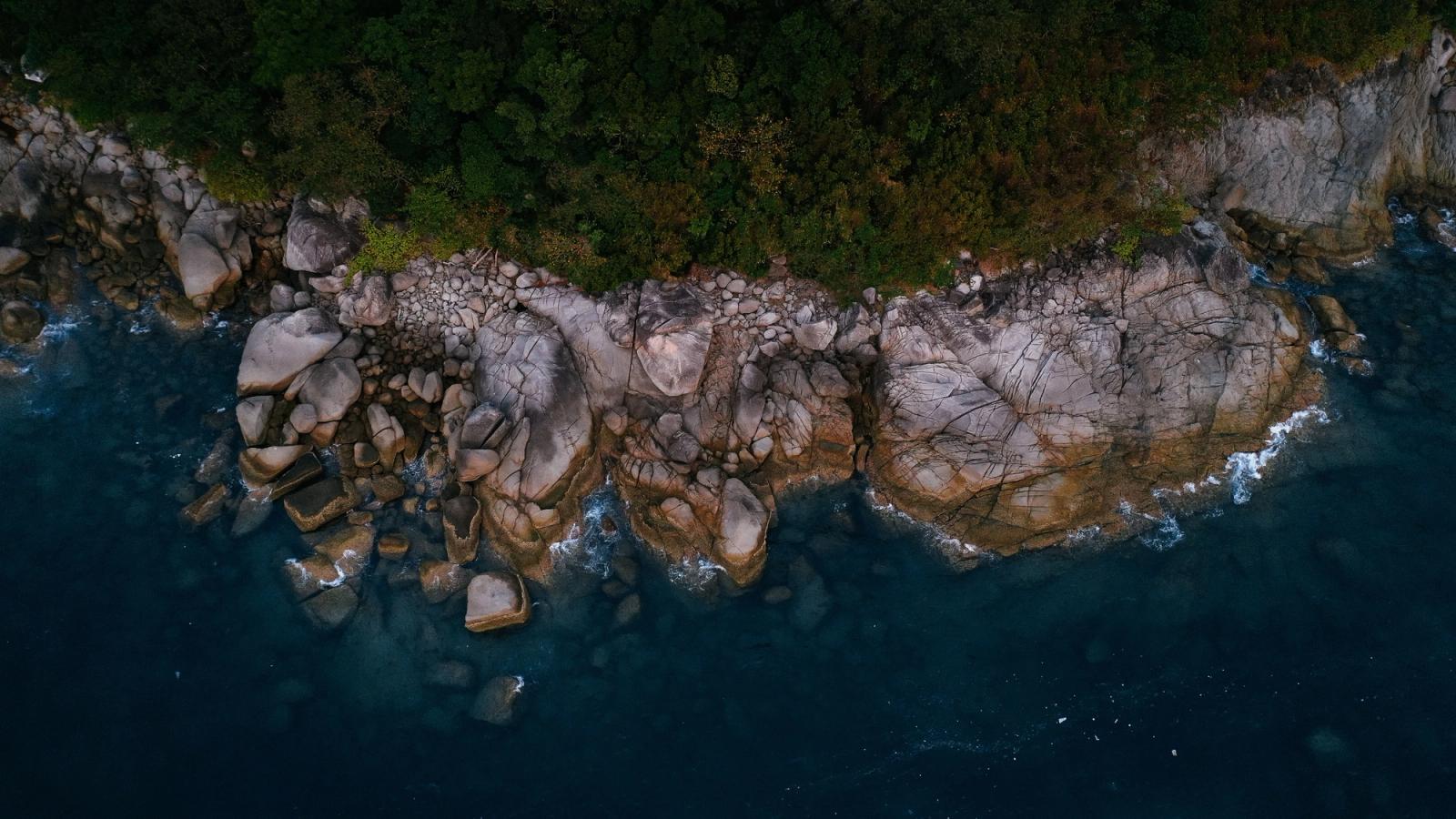 Aerial view of Phuket's rocky coastline and lush greenery meeting the deep blue sea