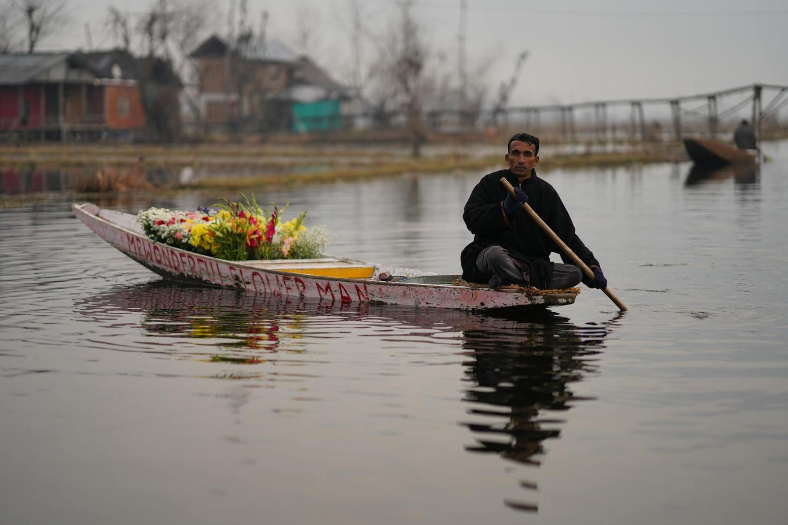 A man paddles a flower-laden boat across a misty lake