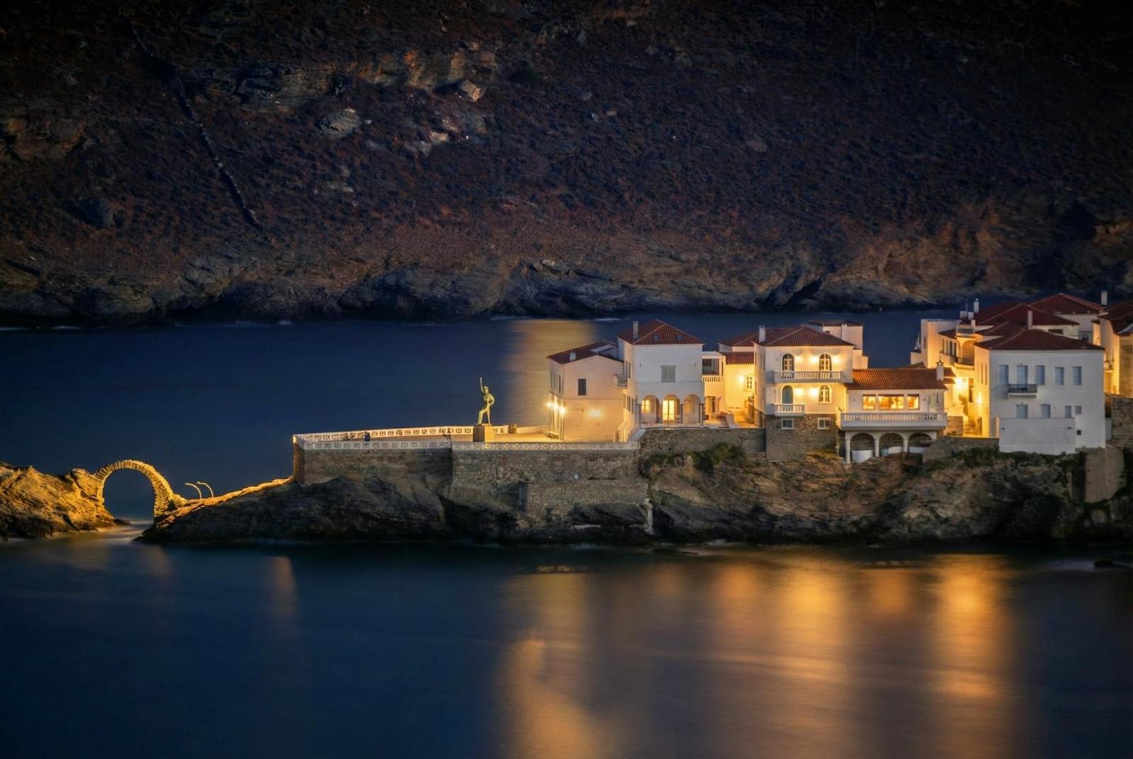 A cliffside village lit up at night beside a stone sea arch