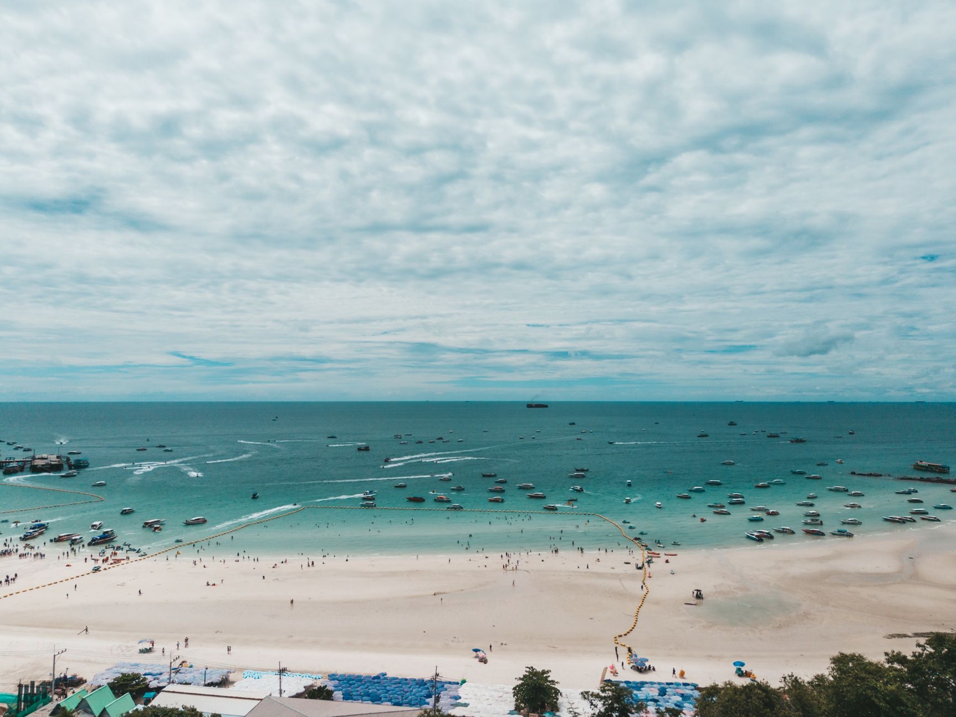 Aerial view of a crowded sandy beach with boats anchored offshore