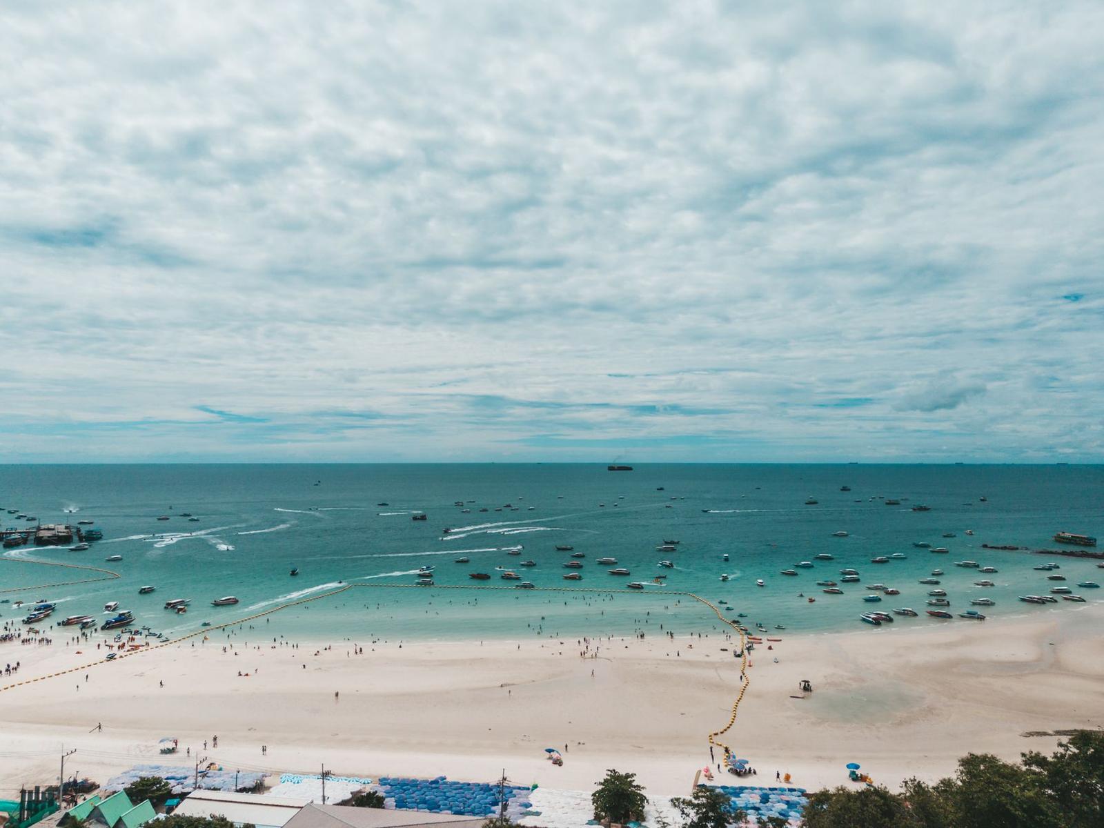 Aerial view of a crowded sandy beach with boats anchored offshore