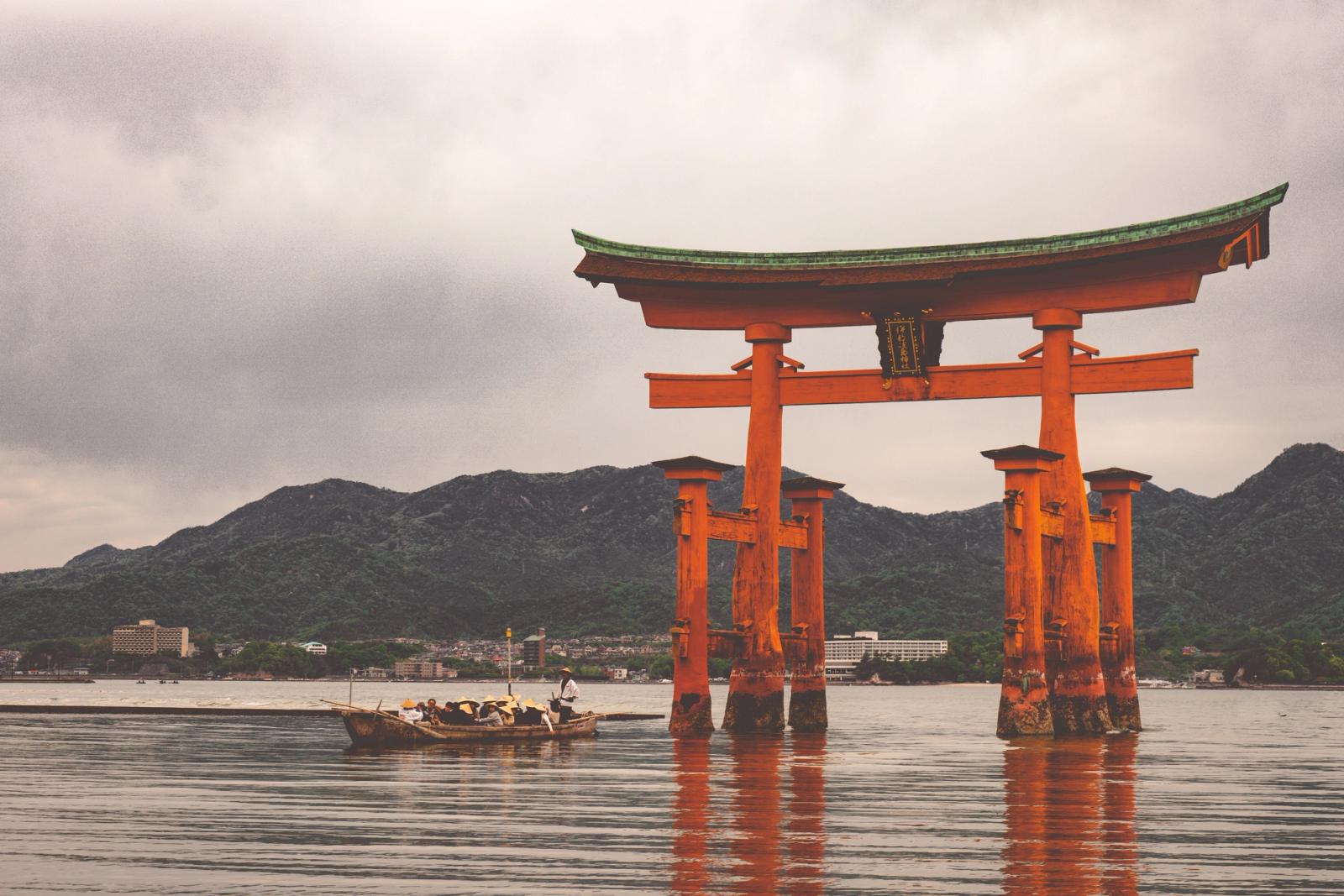 A floating red torii gate in calm water with a small boat passing by