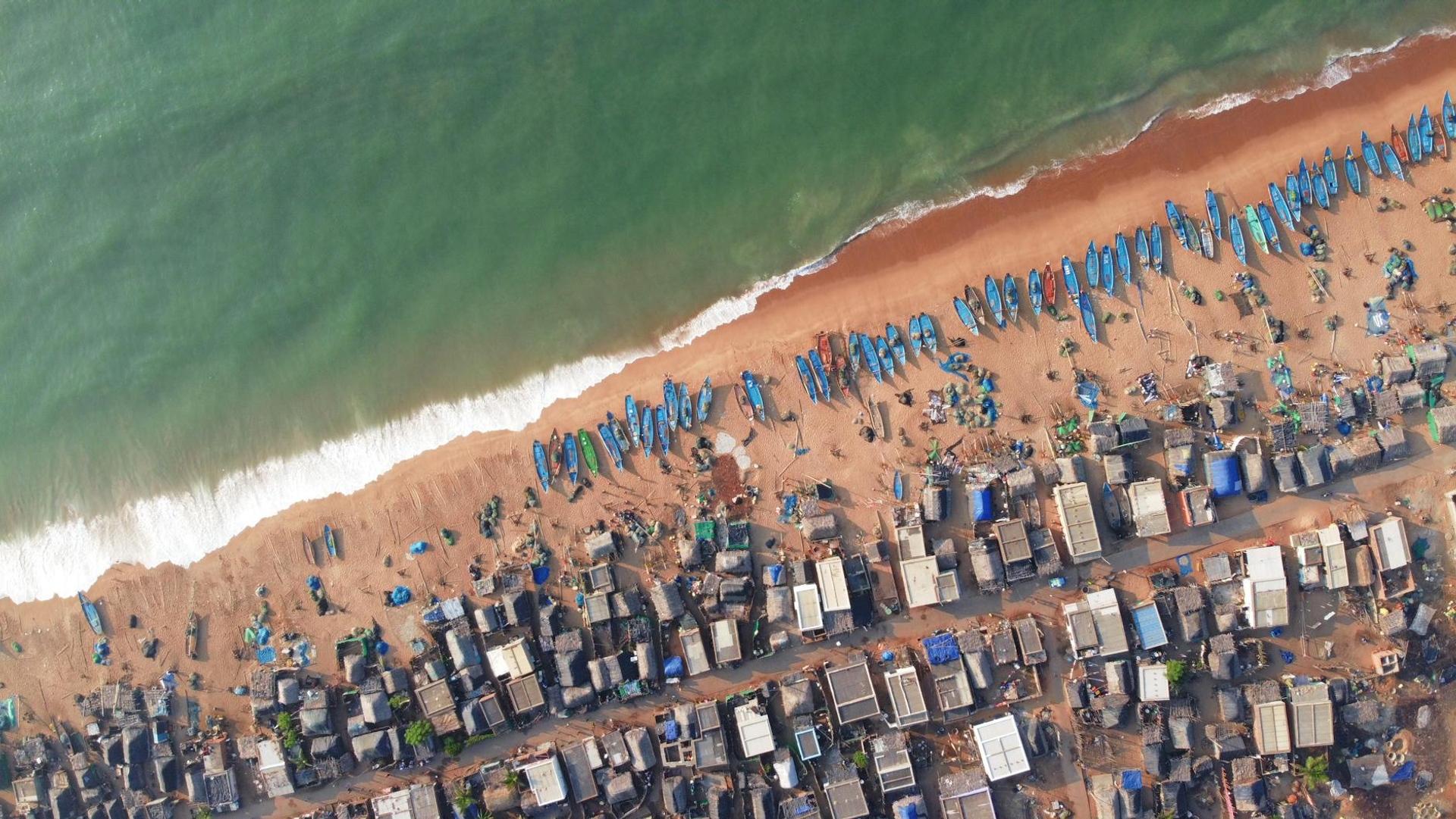 An aerial view of fishing boats lined along a sandy village beach