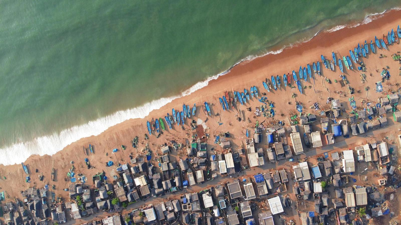 An aerial view of fishing boats lined along a sandy village beach